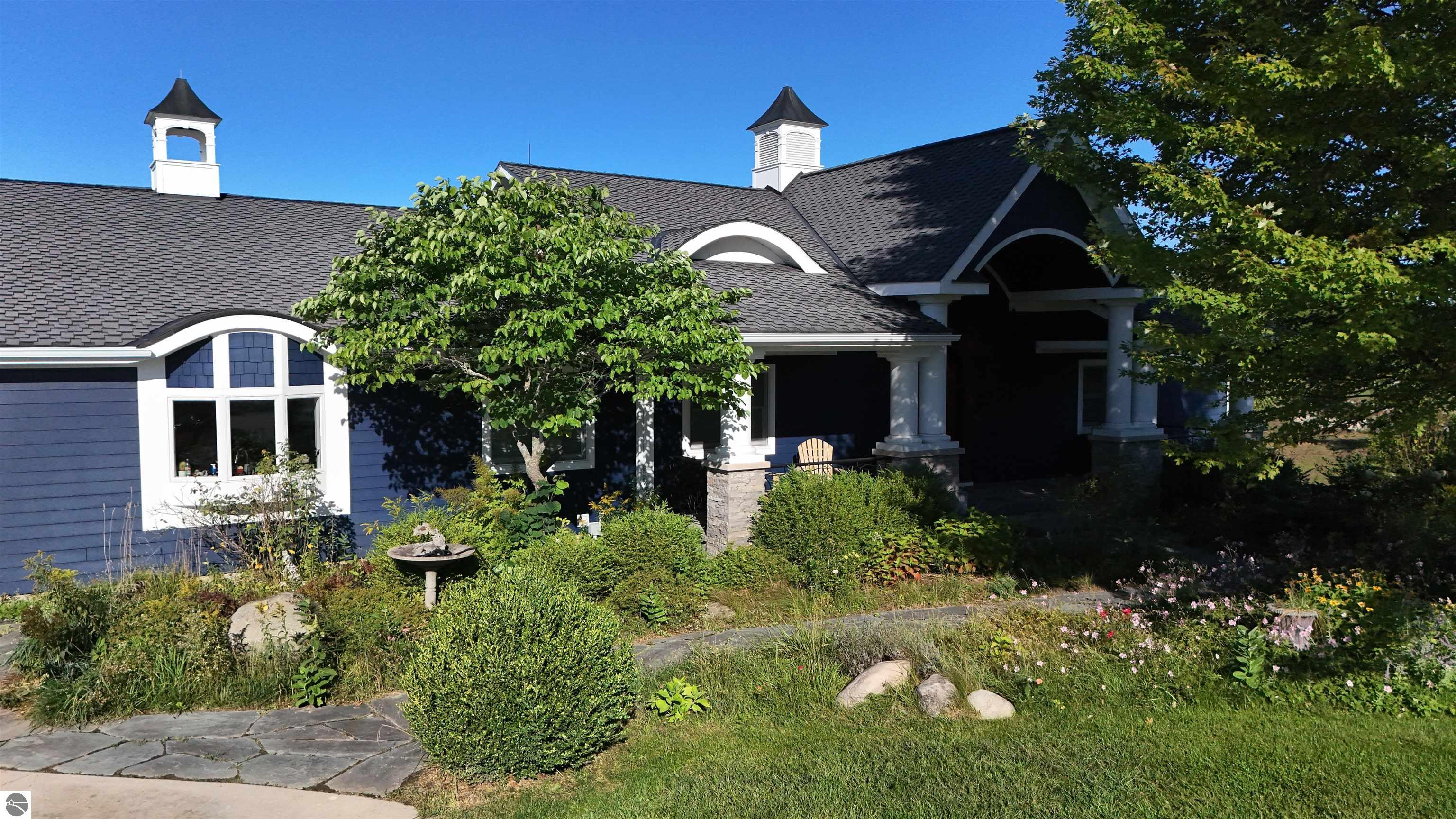 Blue-gray house with white trim, arched windows, roof cupolas, and a landscaped front garden.