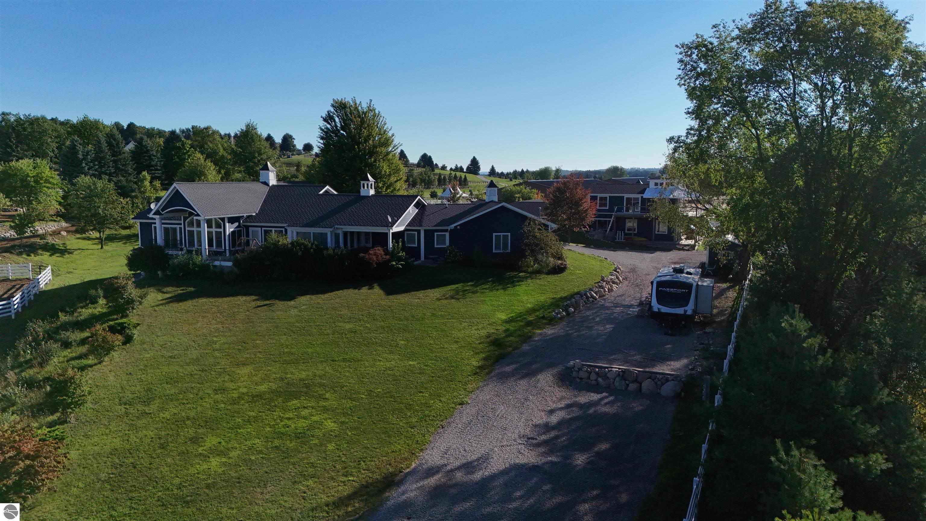 Aerial view of a dark-sided home, broad lawn, gravel driveway, and travel trailer.