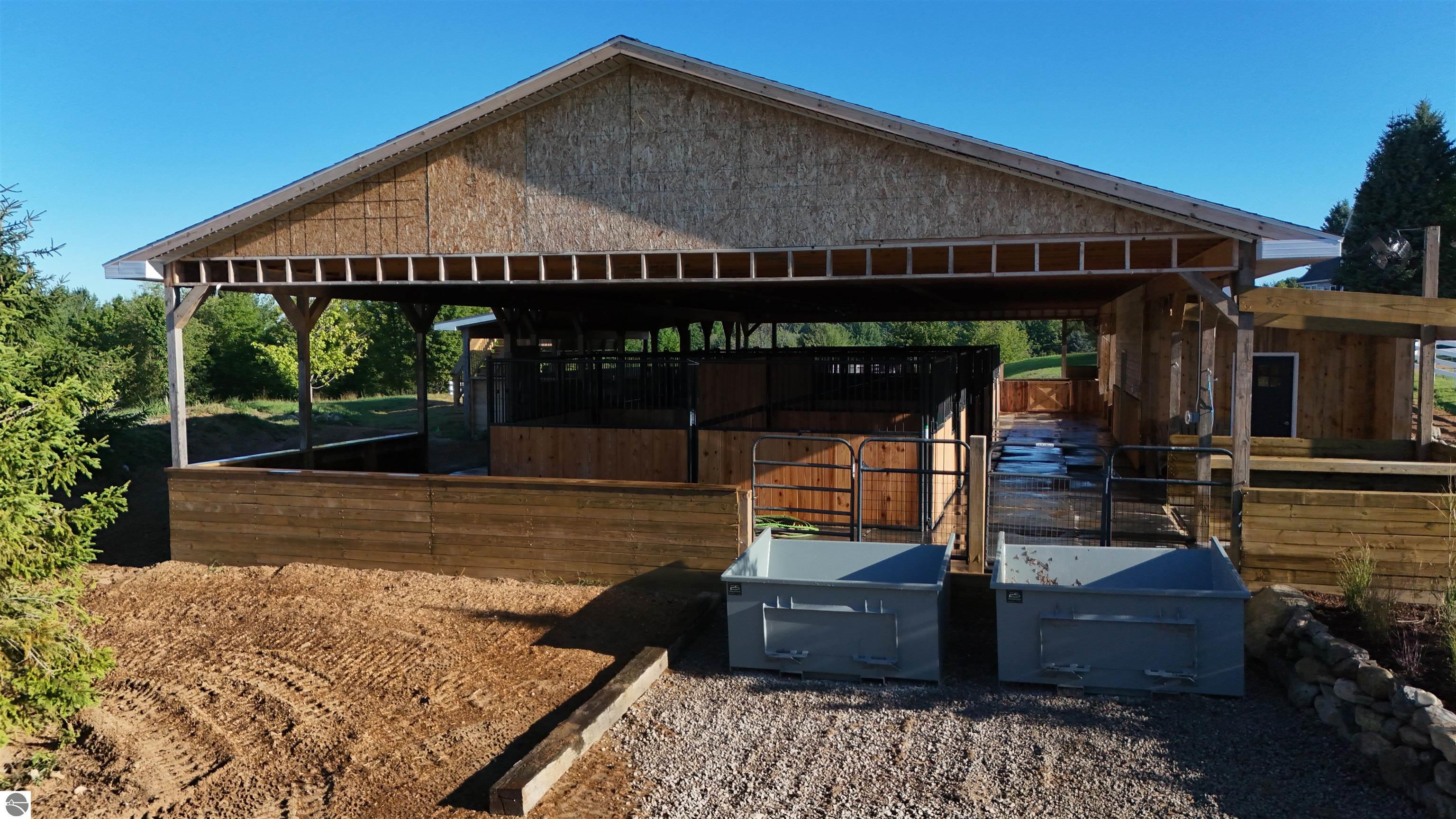 Timber horse barn with fenced stalls, a covered aisle, and two large bins outside.