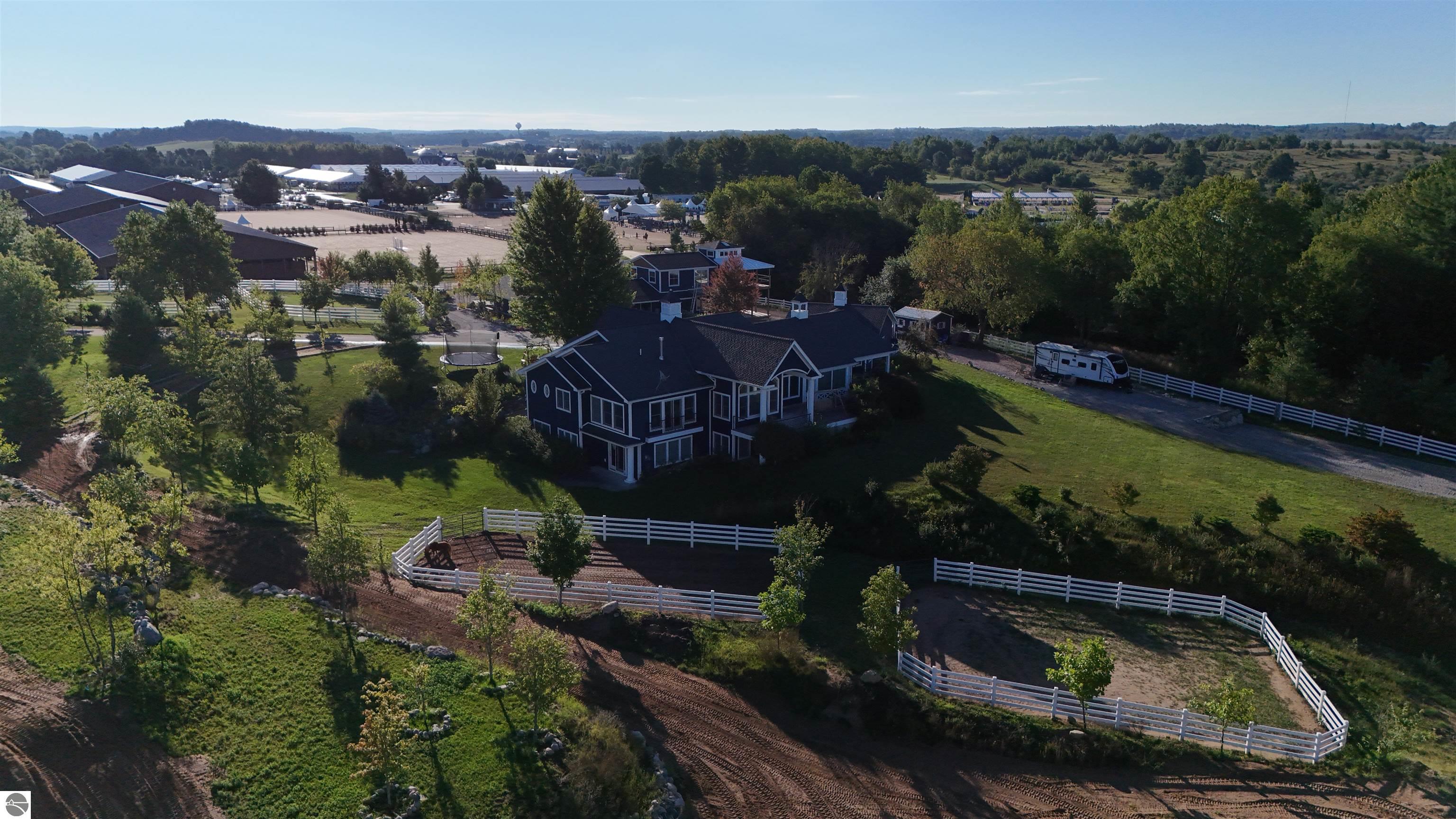 Aerial view of a dark home surrounded by white-fenced paddocks, with equestrian arenas and barns nearby.