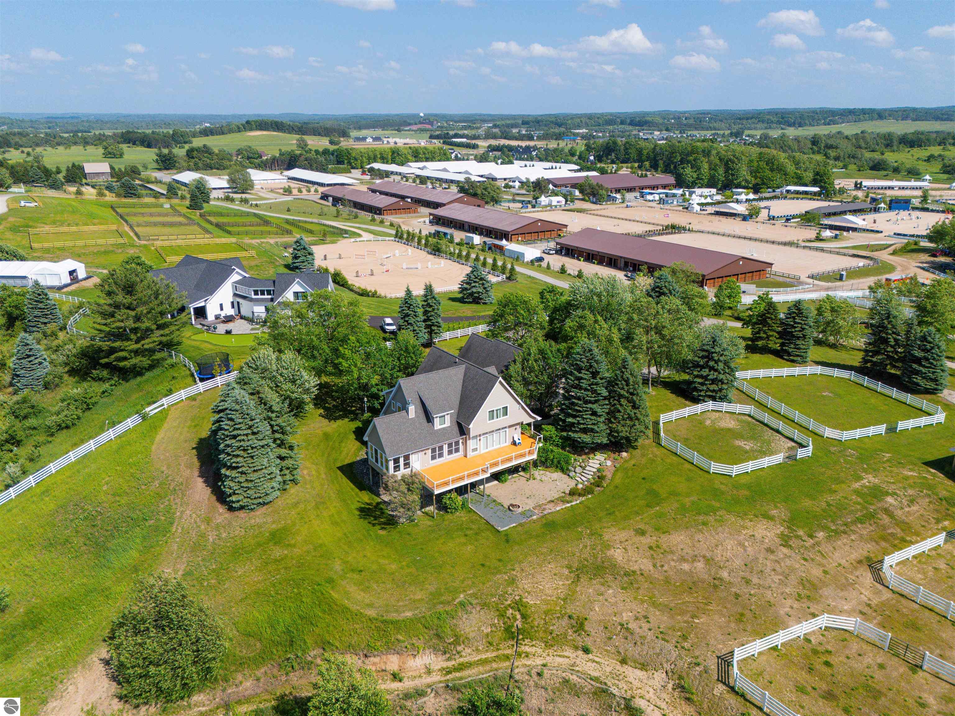 Aerial view of two homes, fenced paddocks, and a large equestrian facility with barns and riding arenas.