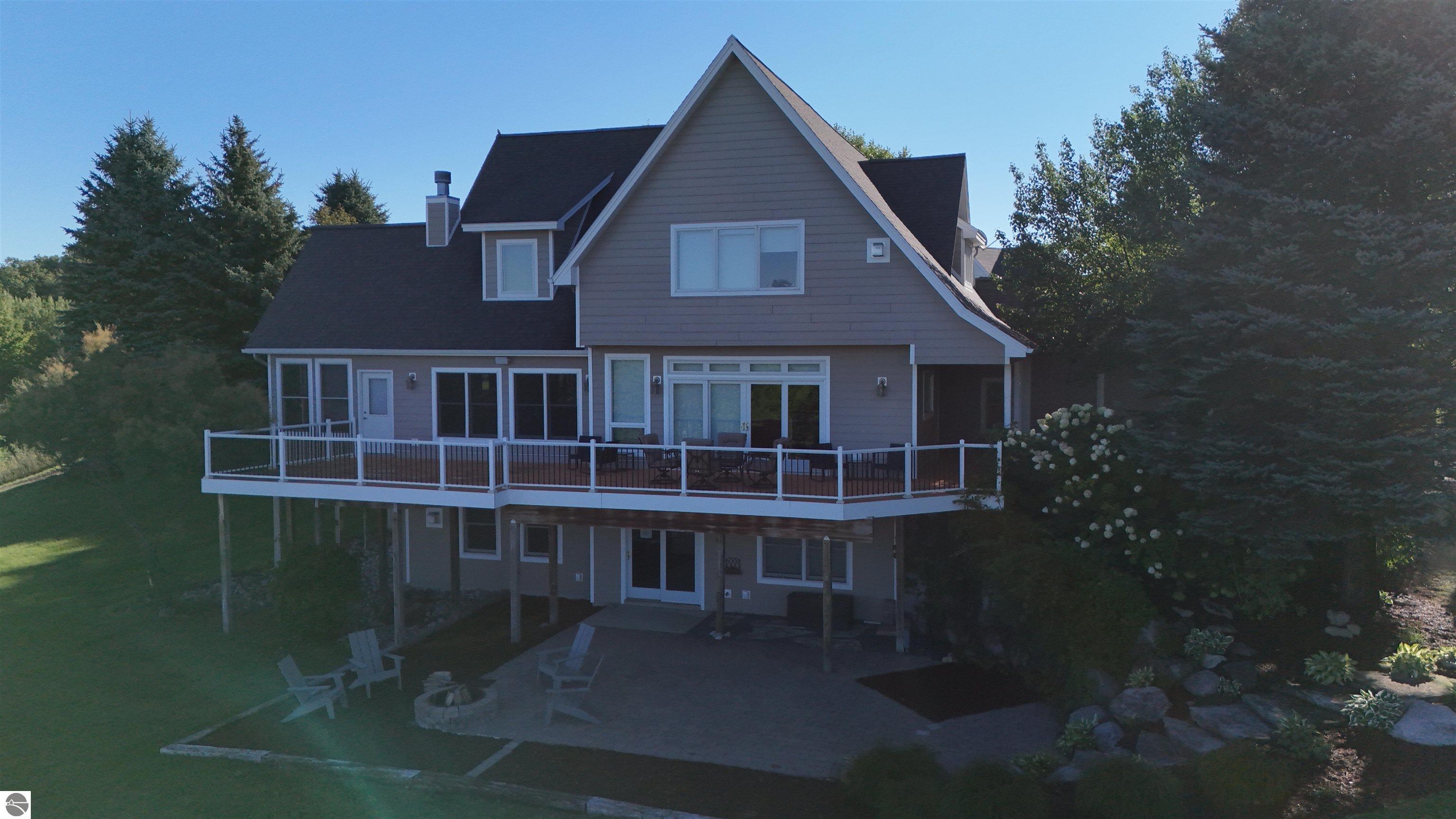 Rear of a gray two-story house with a raised deck above a patio and stone fire pit.