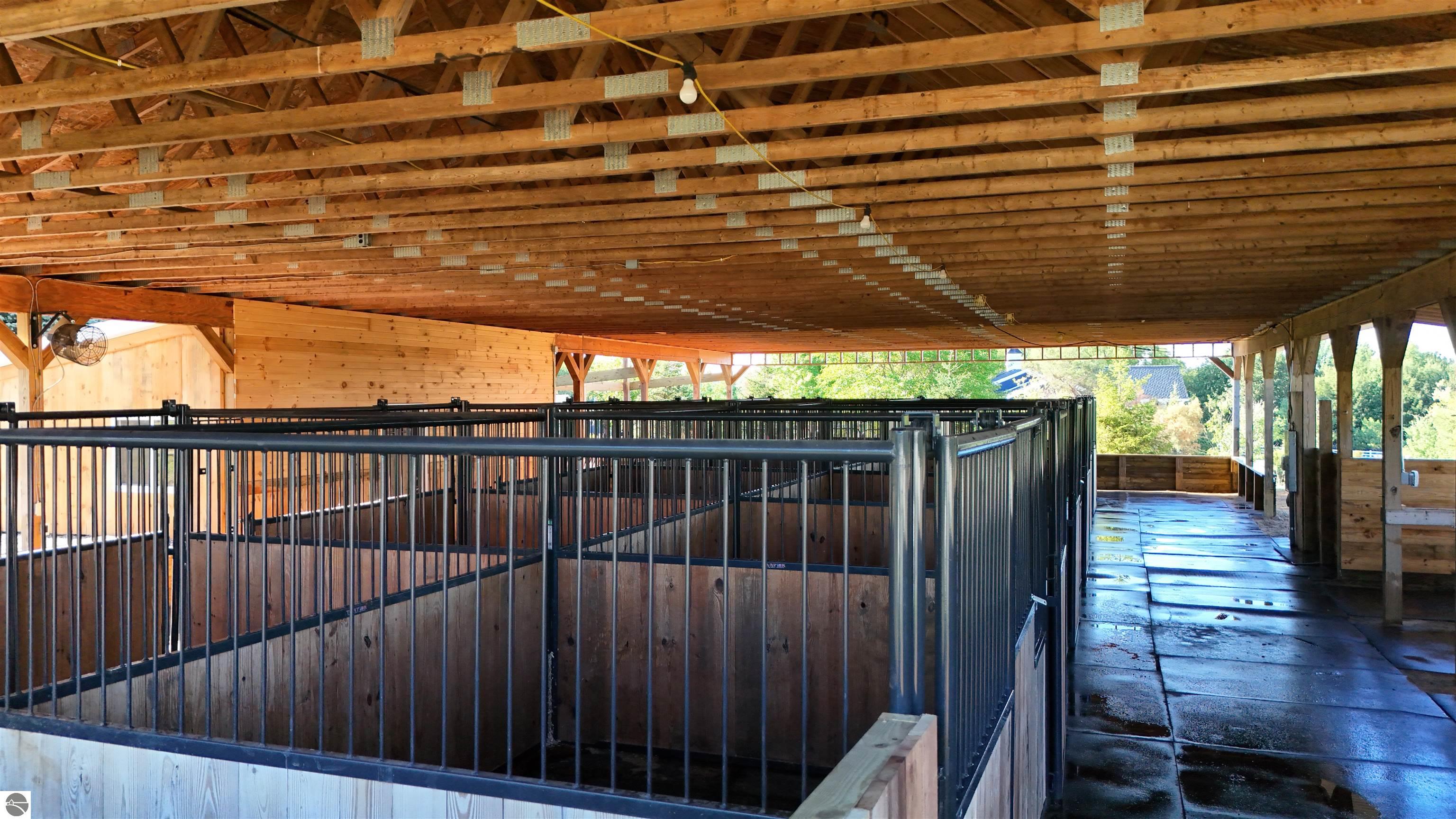 Covered horse barn with empty wood-paneled stalls, black metal gates, and a wet concrete aisle.