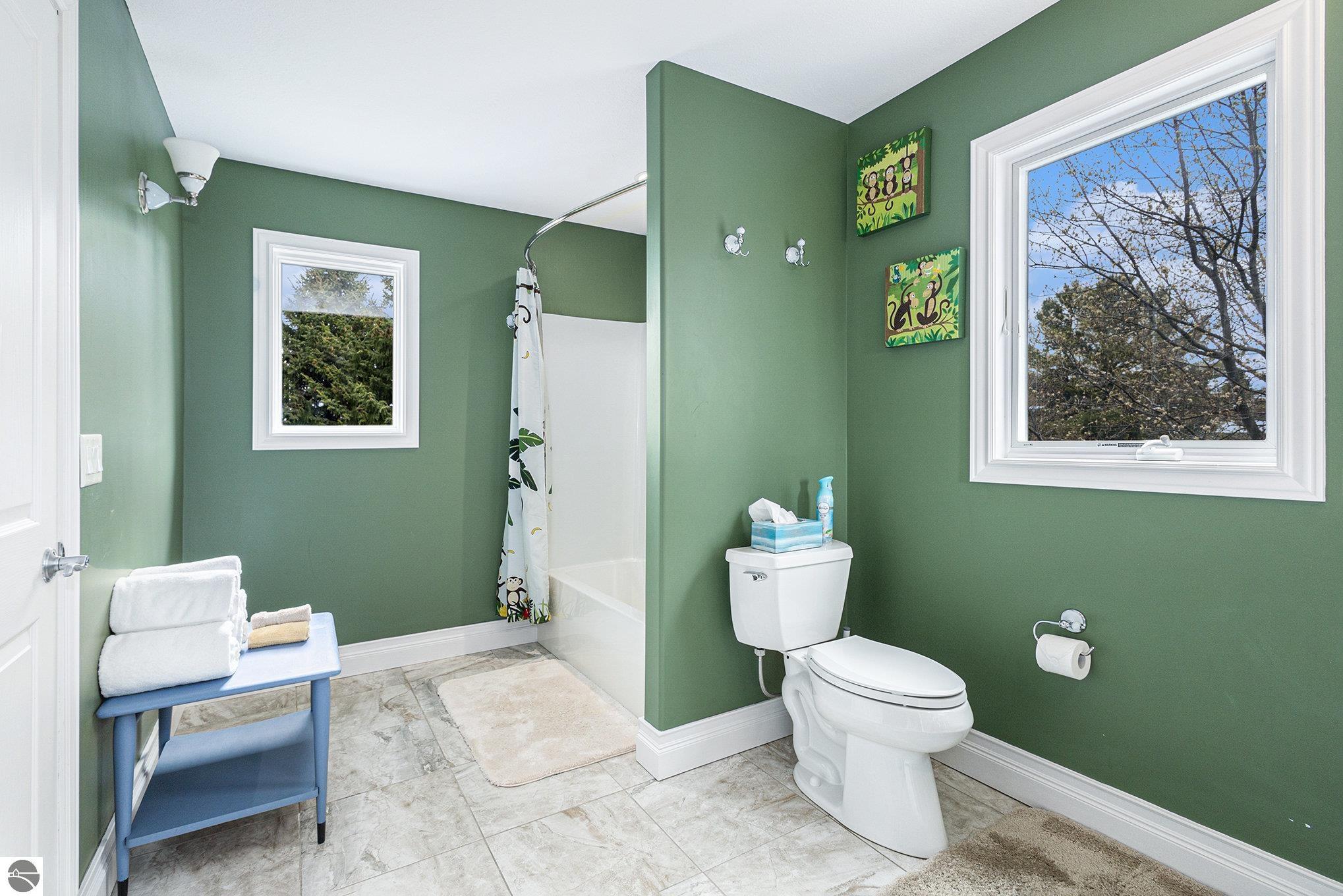 Bathroom with sage-green walls, tiled floor, white fixtures, and two windows.