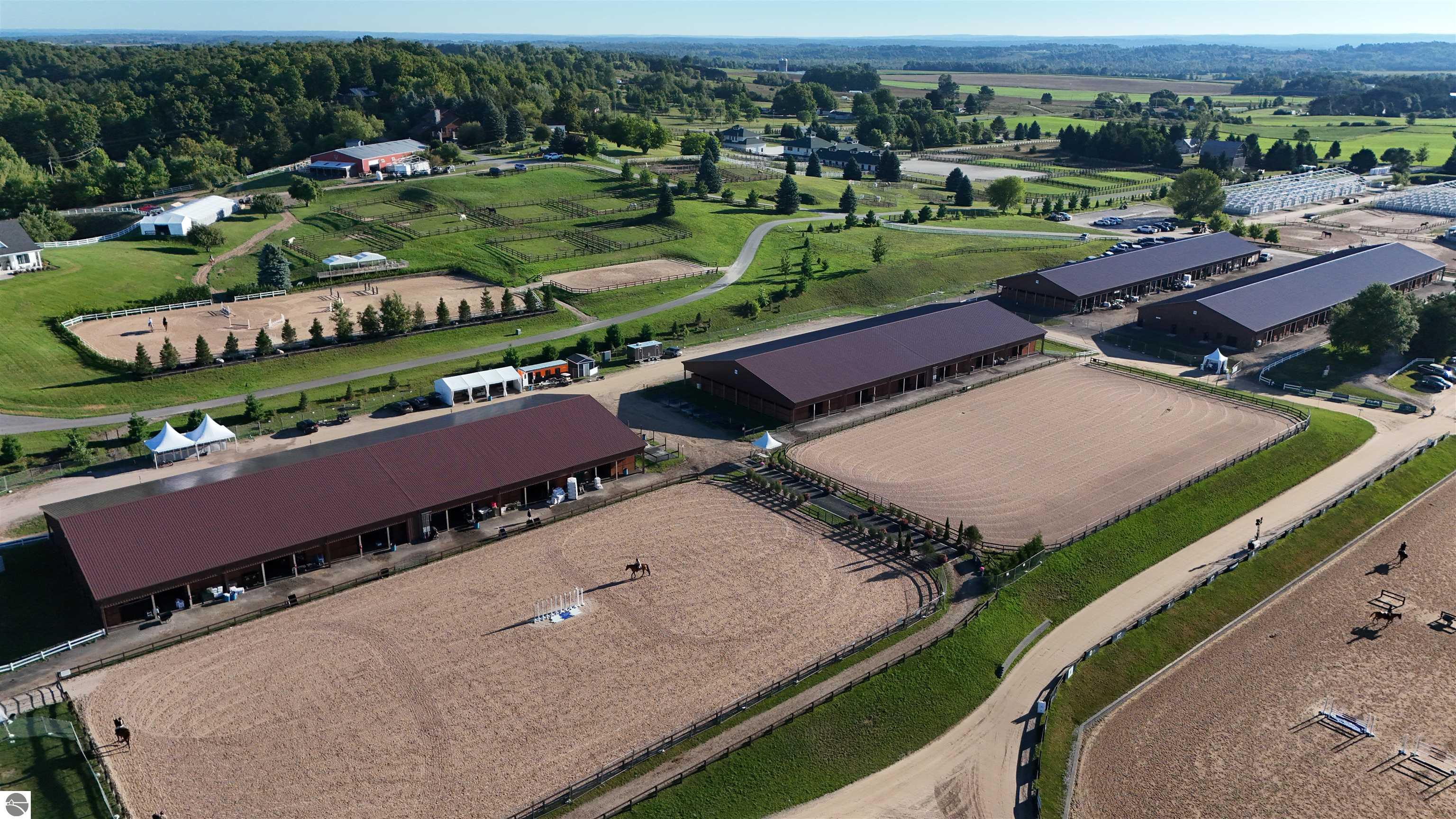 Aerial view of an equestrian facility with multiple barns, outdoor arenas, and fenced paddocks.