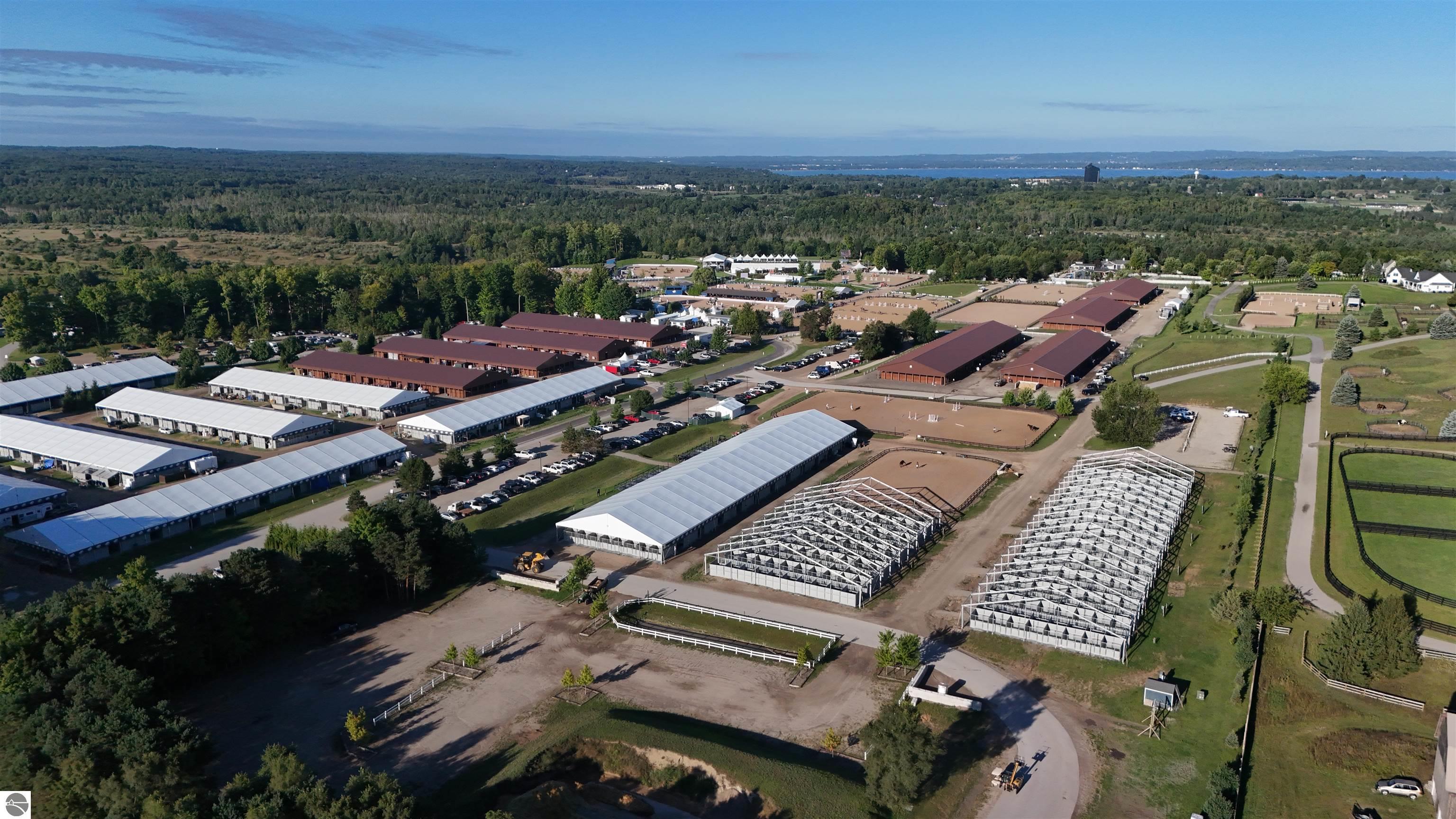 Aerial view of an equestrian complex with barns, riding arenas, paddocks, and a distant lake.