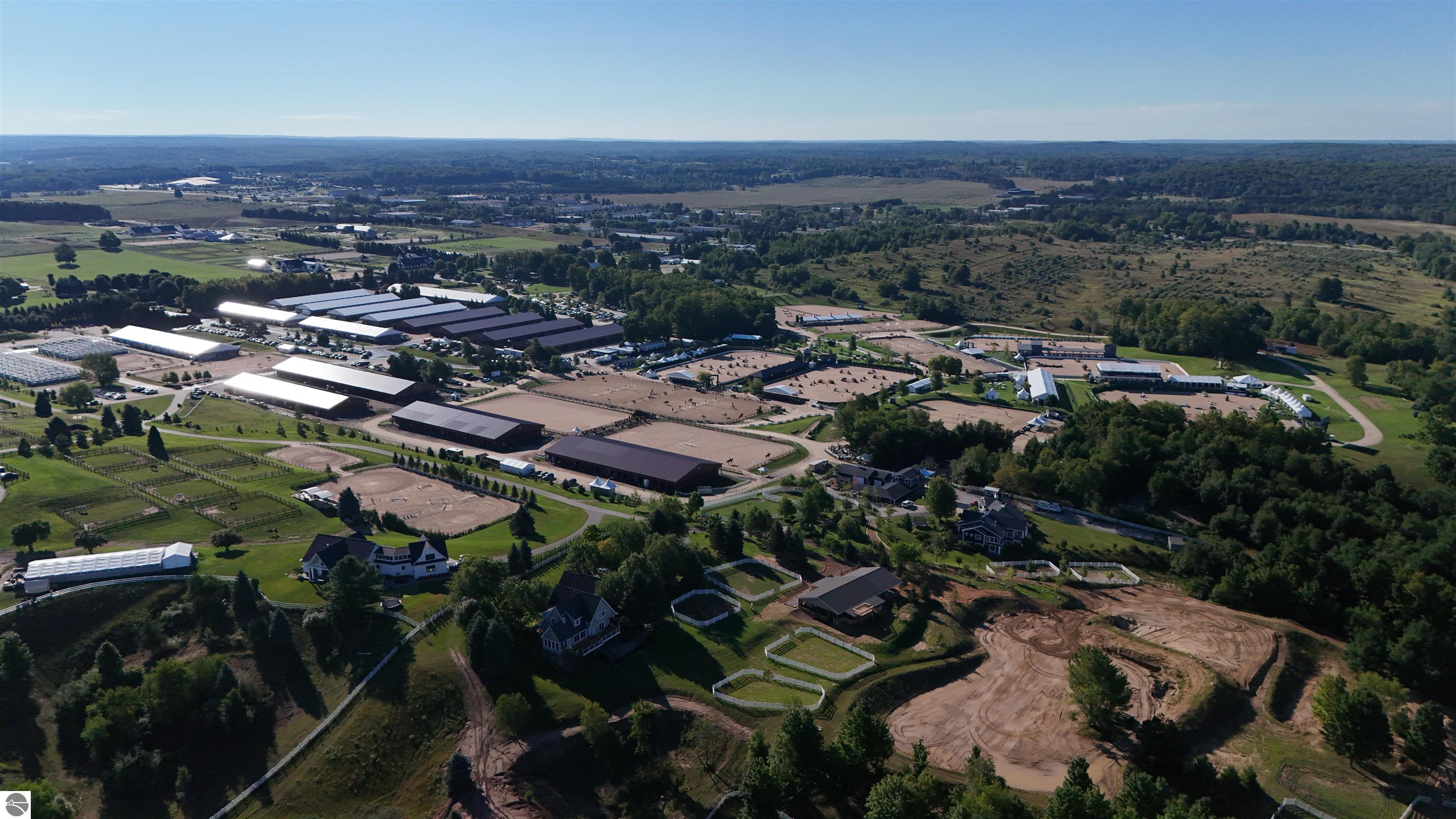 Aerial view of an equestrian complex with large barns, riding arenas, fenced paddocks, and homes.