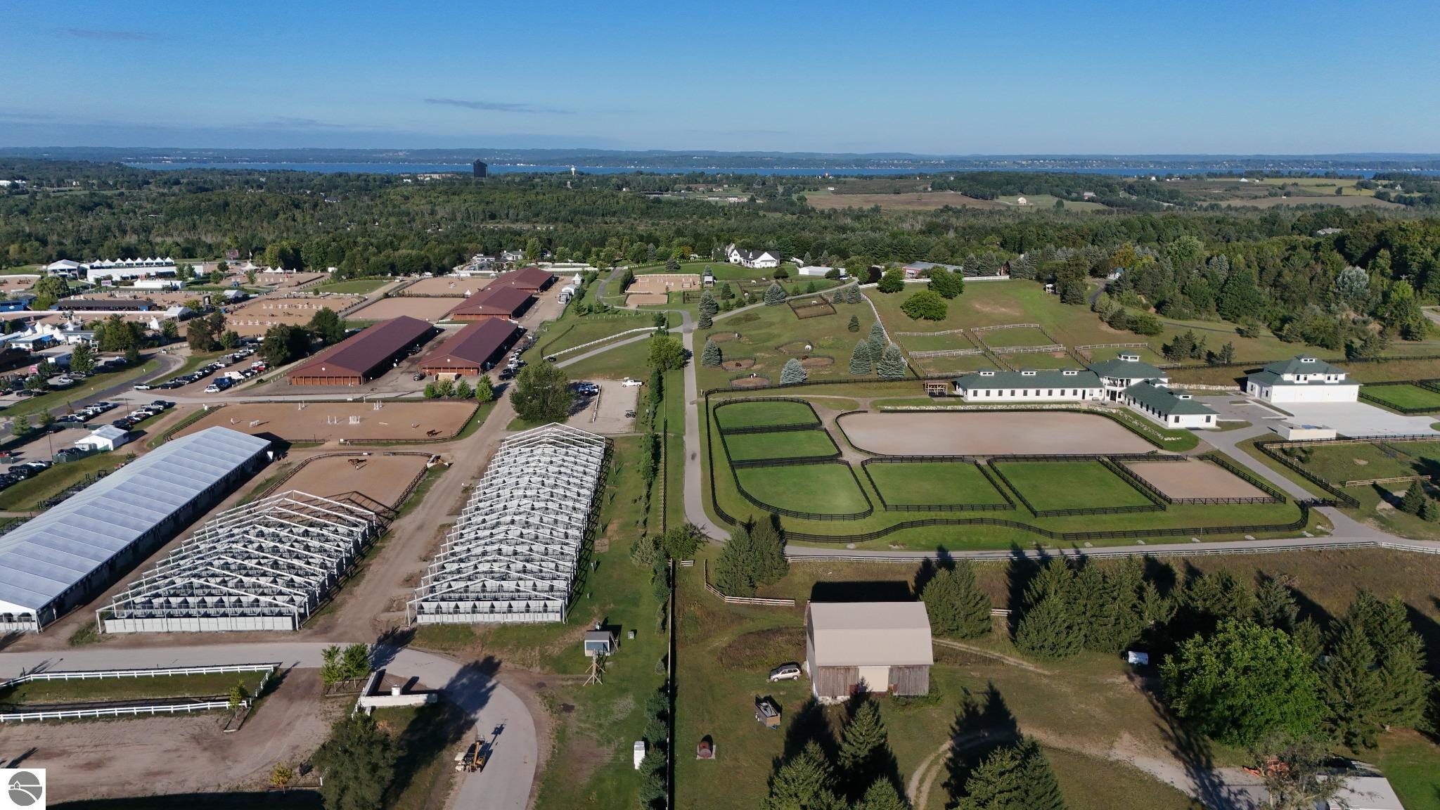Aerial view of an equestrian facility with barns, arenas, paddocks, and a distant lake.
