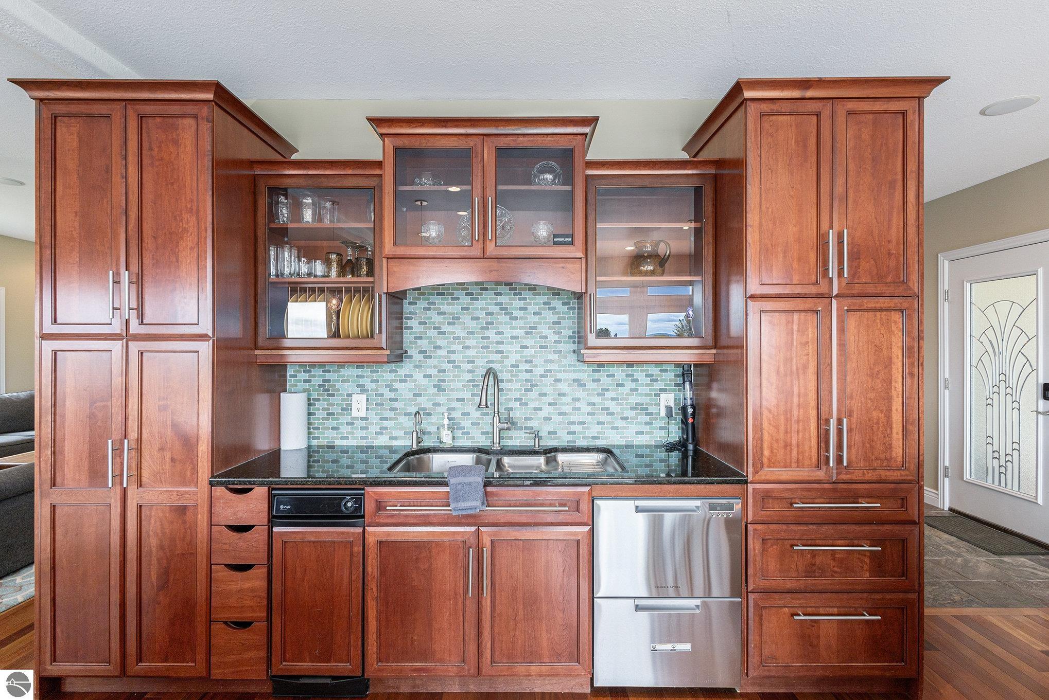 Kitchen with reddish wood cabinetry, glass-front cupboards, a blue-green tile backsplash, and stainless steel appliances.