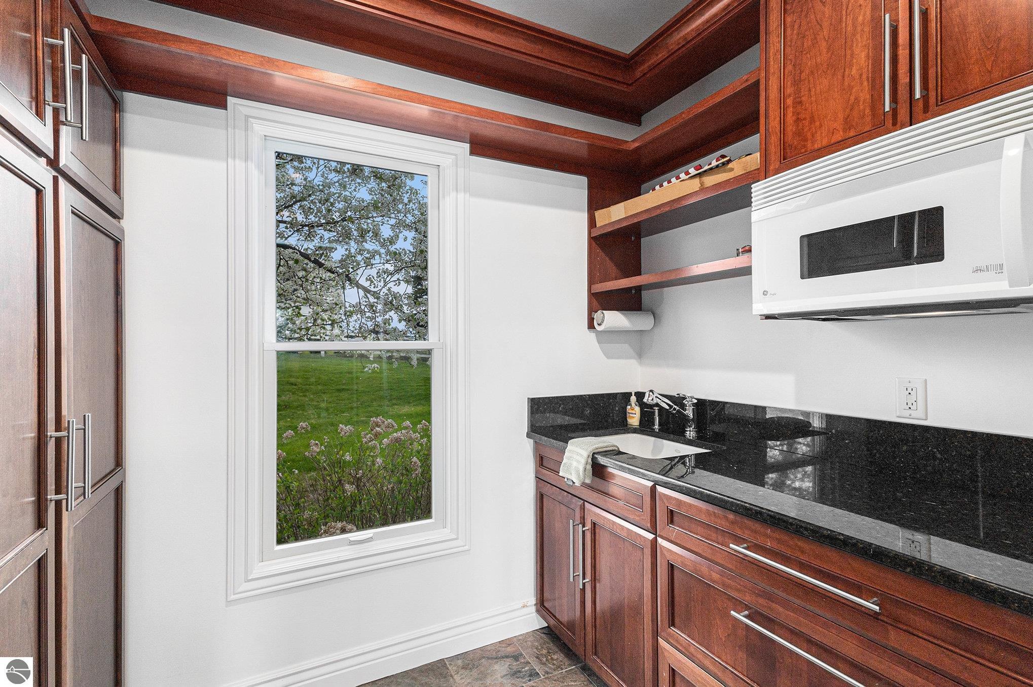 Kitchen with reddish wood cabinetry, black countertops, a sink, and a window overlooking flowering trees.