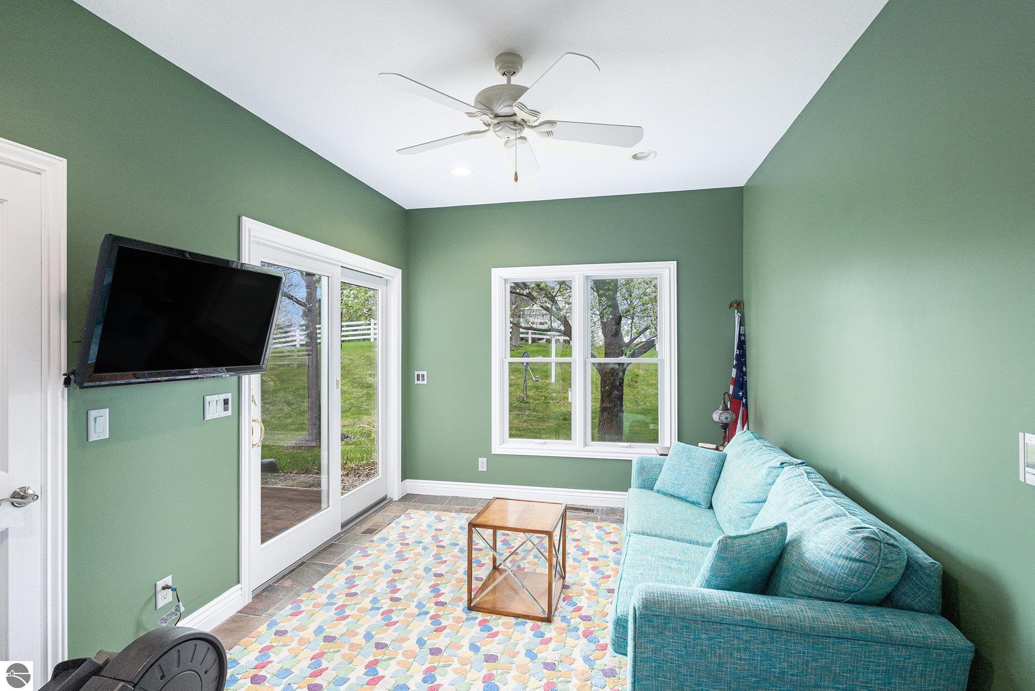 Sunroom with green walls, a blue sectional, colorful rug, and glass doors overlooking a fenced yard.