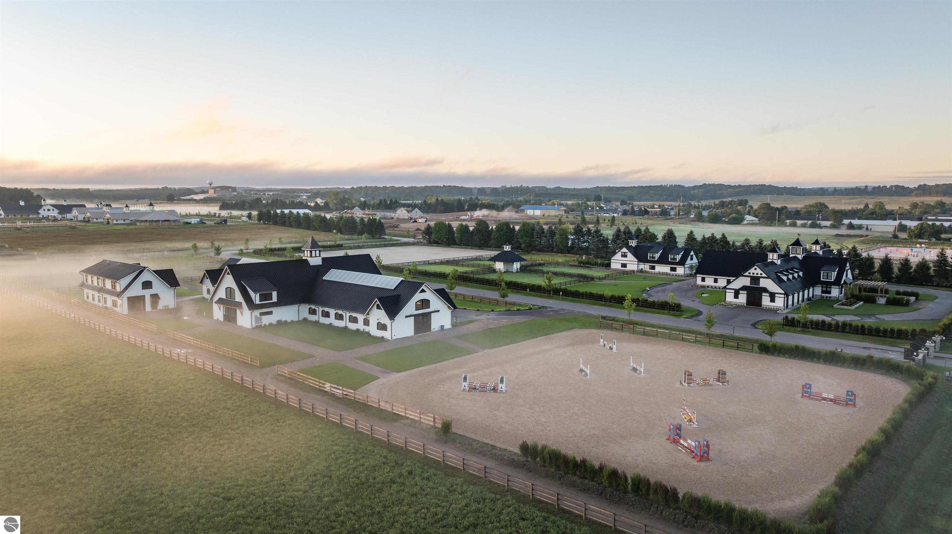 Aerial view of an equestrian estate with white barns, fenced paddocks, and a show-jumping arena.