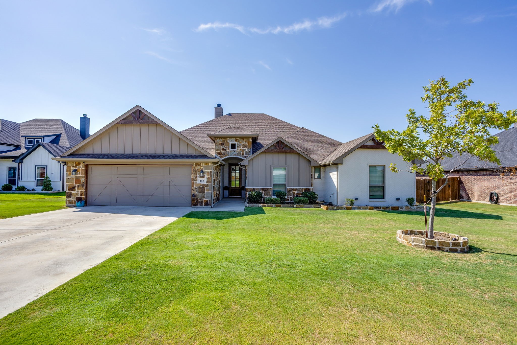 Single-story home with stone accents, a wide two-car garage, and a broad green lawn.