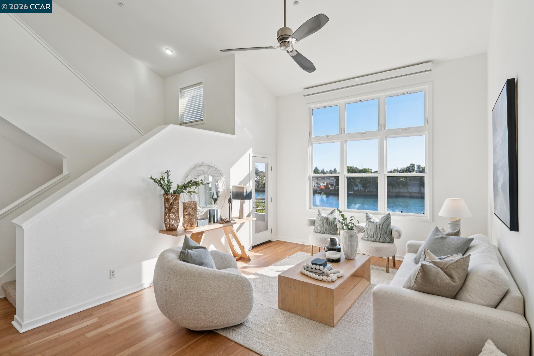 Staged living room with a staircase and large windows overlooking the water.