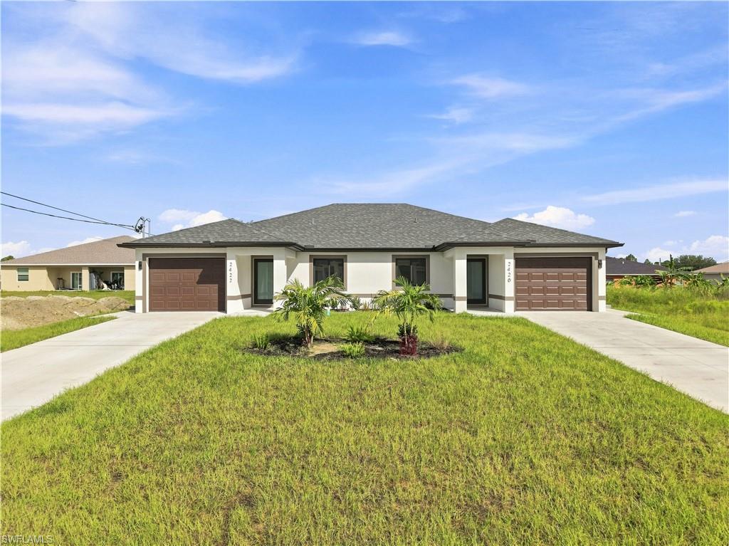 Single-story duplex with two garage doors, separate driveways, and a lawn with small palms.