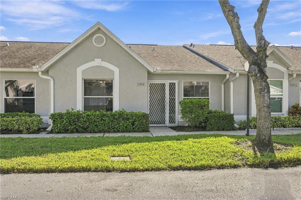 Gray stucco townhouse with a peaked roof, gated entrance, trimmed hedges, and a front lawn.