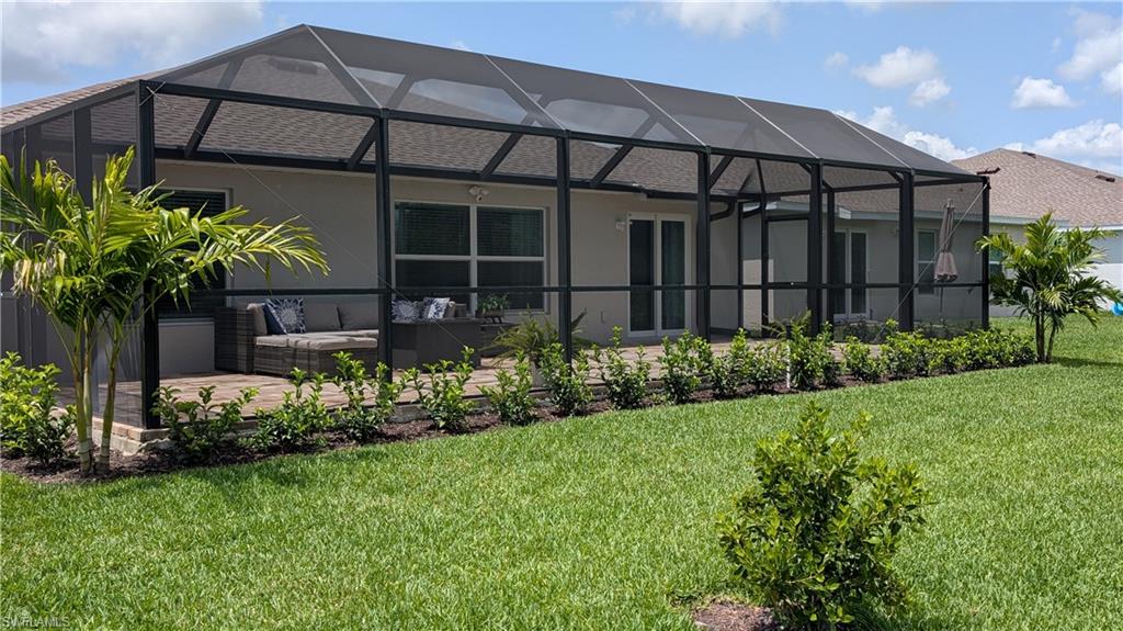 Home’s screened lanai with patio seating, tropical landscaping, and a broad green lawn.