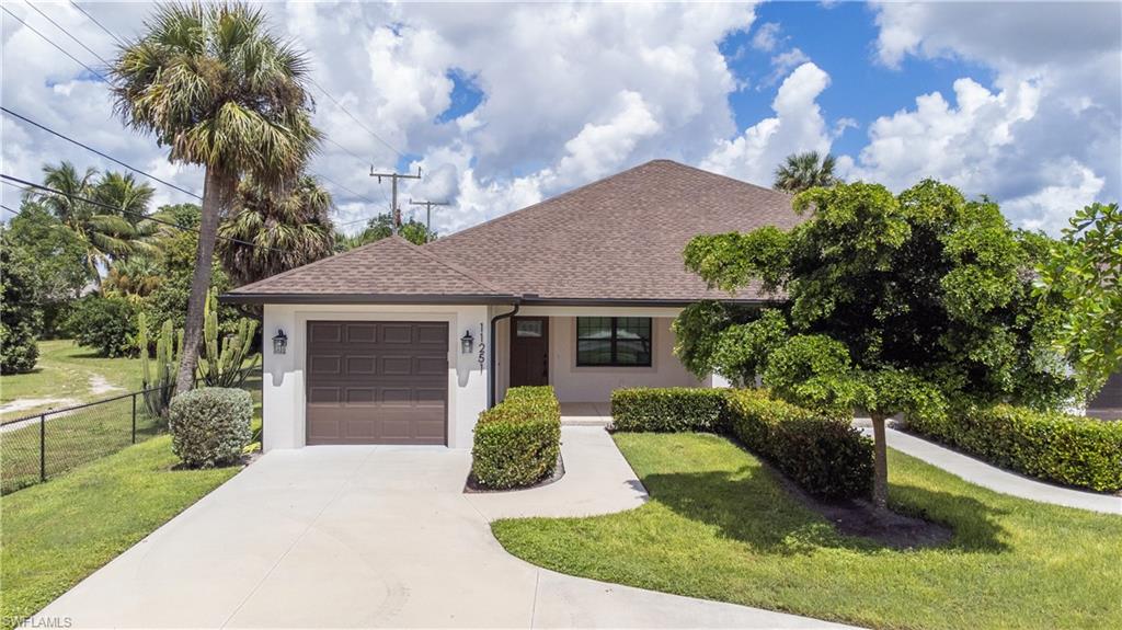 Single-story house with an attached garage, curved driveway, and landscaped lawn with palms.