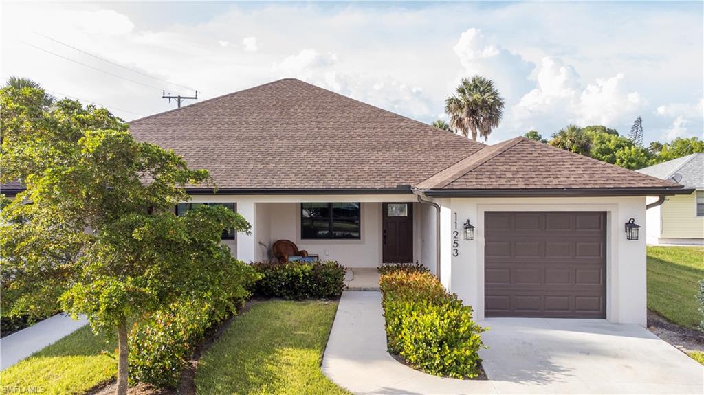 Single-story white home with an attached garage, brown shingle roof, and leafy tree by the front walk.