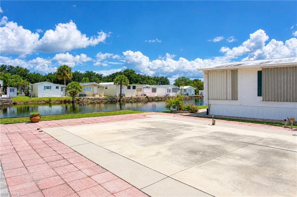 Paved patio beside a manufactured home, overlooking a canal and neighboring homes.