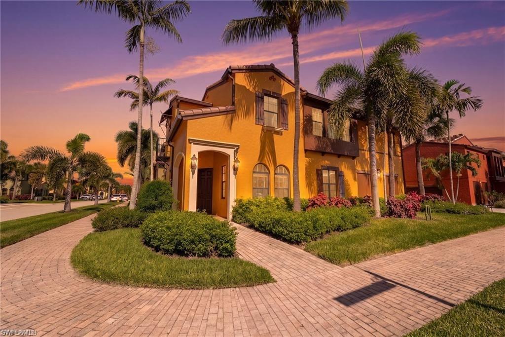 Two-story orange stucco home with palm trees and a curved brick-paver walkway at dusk.