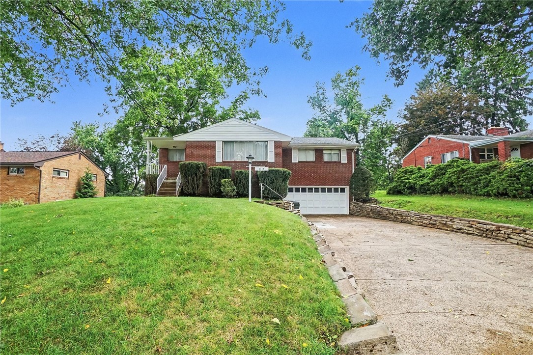 Red-brick split-level home with a sloping lawn, wide driveway, and stone retaining wall.