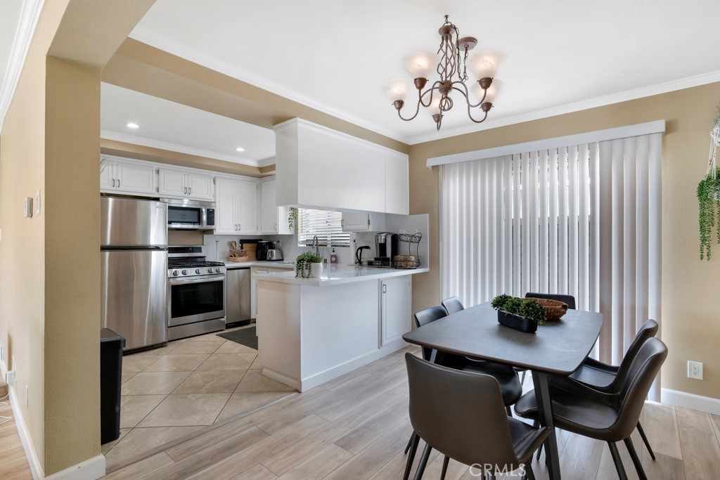 Kitchen and dining area with white cabinets, stainless steel appliances, and a table beneath a chandelier.