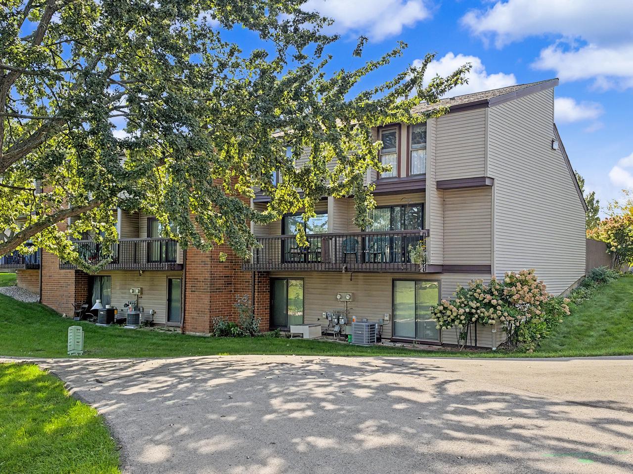 Multi-unit residential building with long balconies, partly screened by a leafy tree.