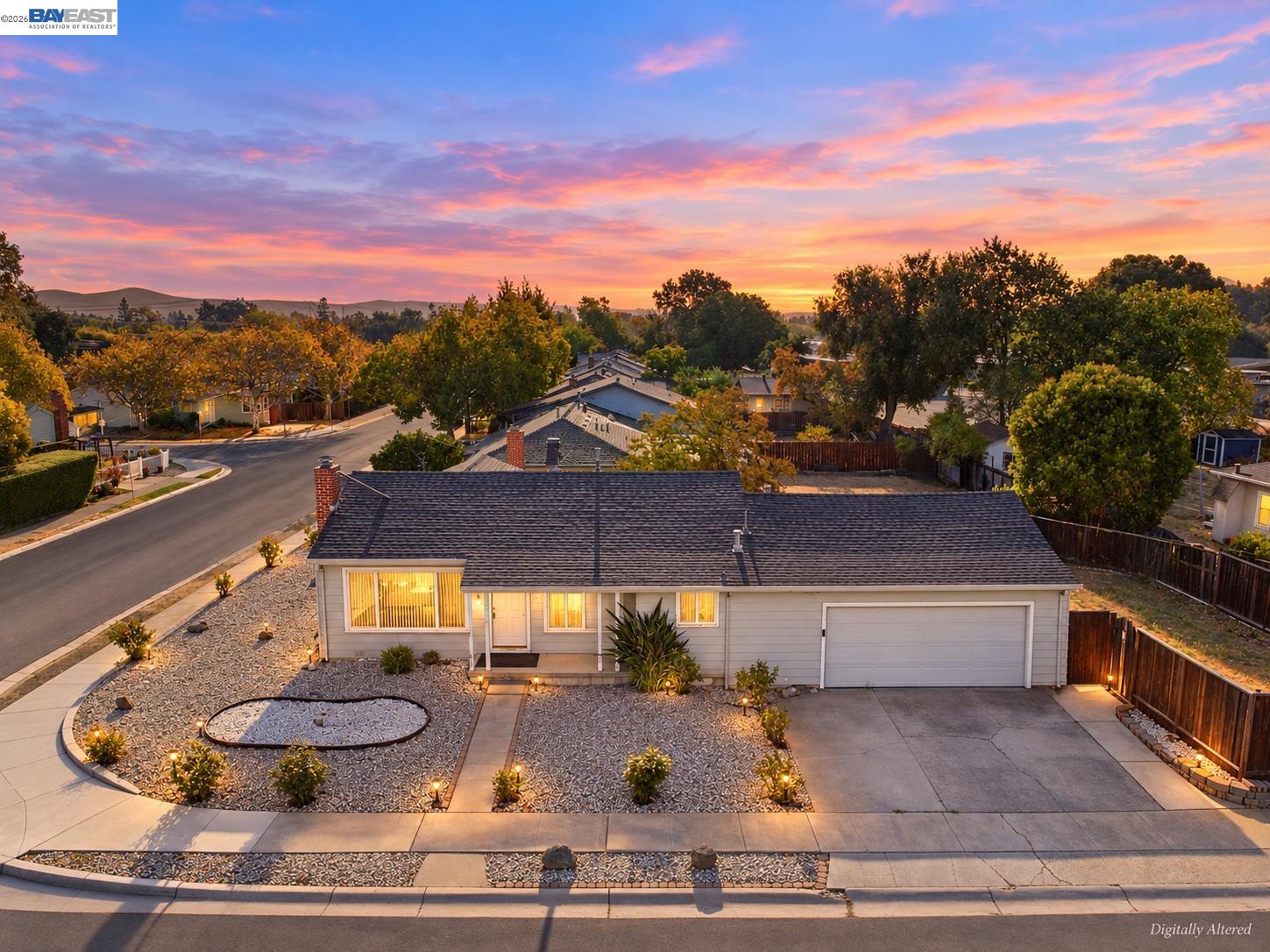 Single-story home with a two-car garage and gravel landscaping beneath a colorful sunset sky.