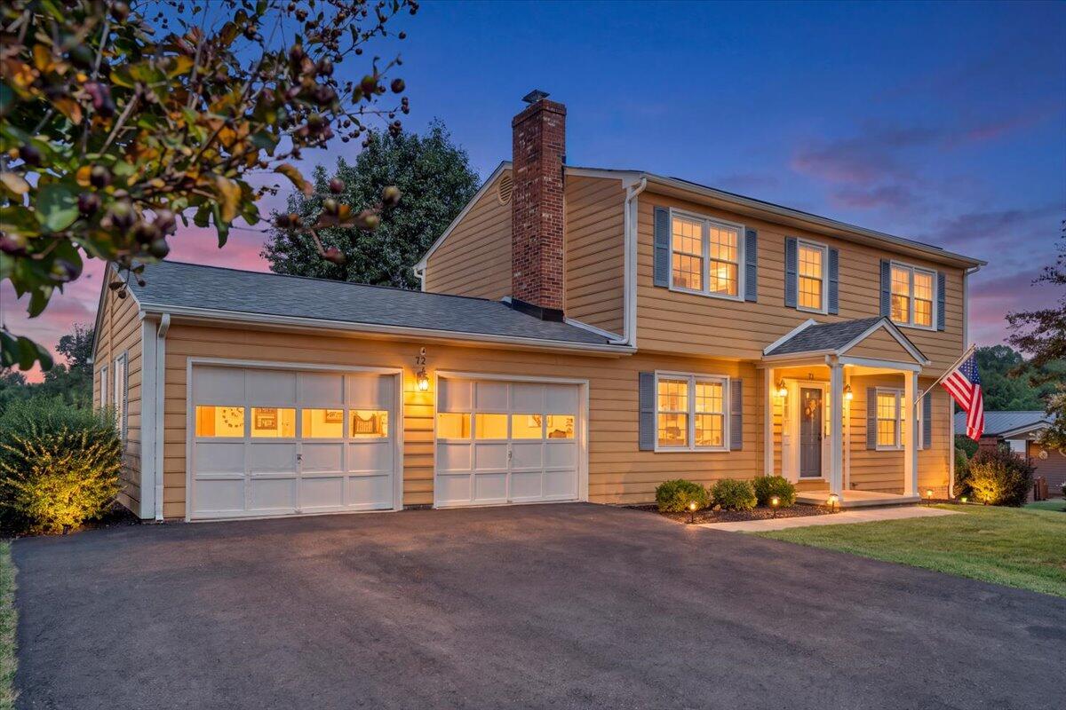Two-story tan home with an attached garage and warmly lit windows at dusk.