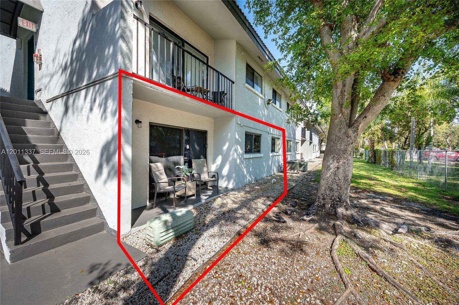 Ground-floor condo exterior outlined in red, with a covered patio and two chairs beside an exterior staircase.
