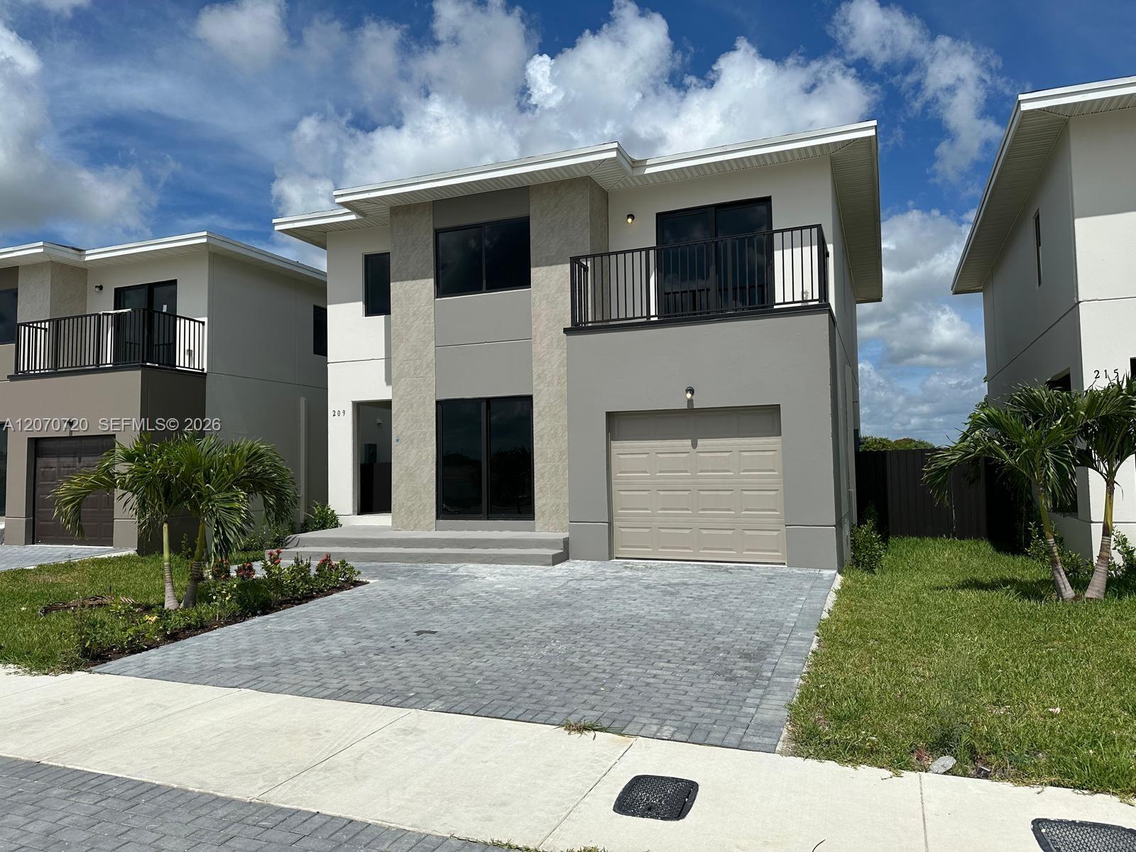 Modern two-story home with a balcony, garage, and paver driveway.