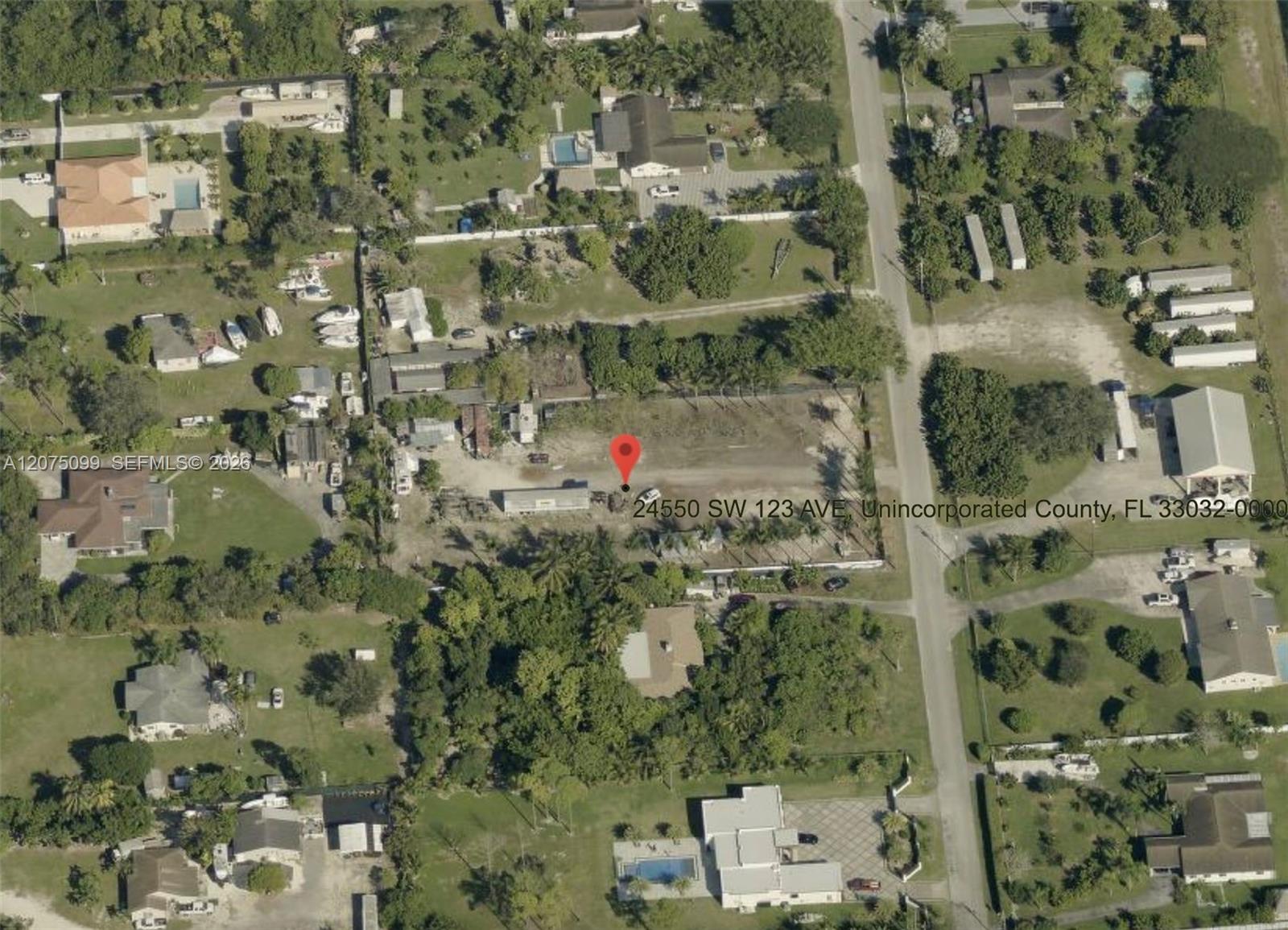 Aerial view of a vacant parcel marked by a red pin, with homes and a road nearby.