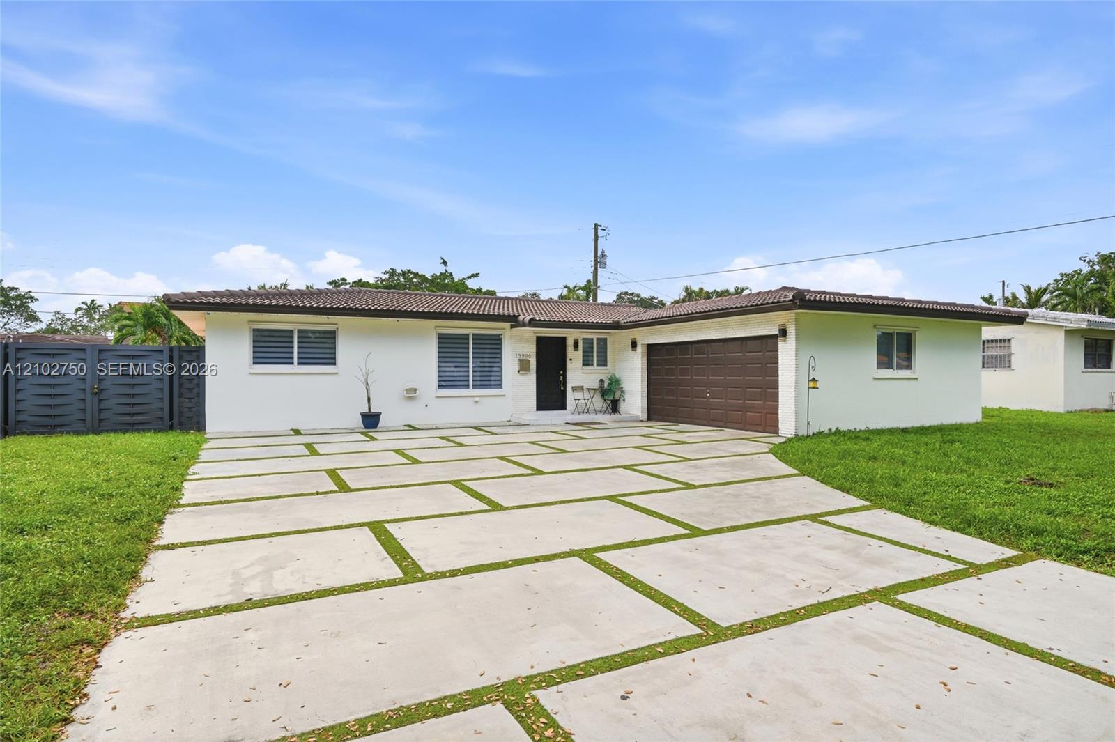Single-story white house with a brown tile roof, attached garage, and broad concrete driveway with grass strips.