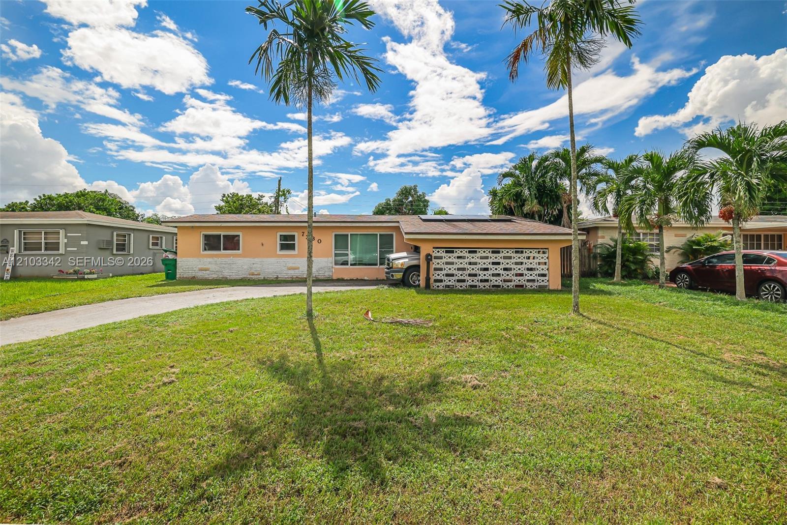 Peach single-story house with a patterned garage door, solar panels, and palm trees across the lawn.