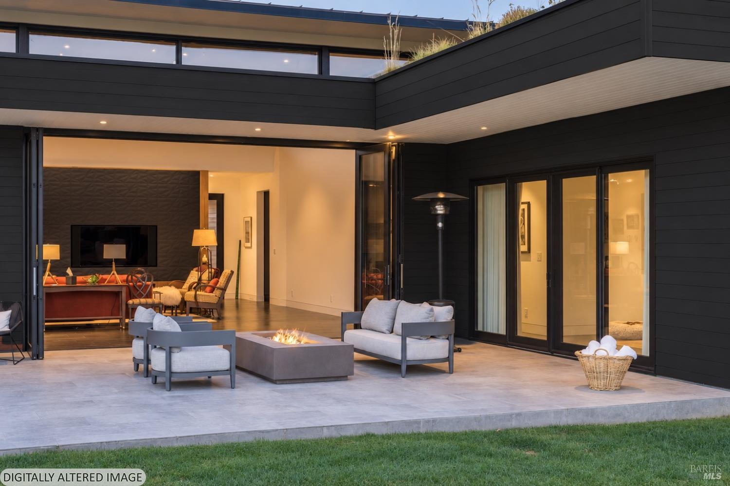 Modern home with an open covered patio, glass doors, lounge seating, and a fire table at dusk.
