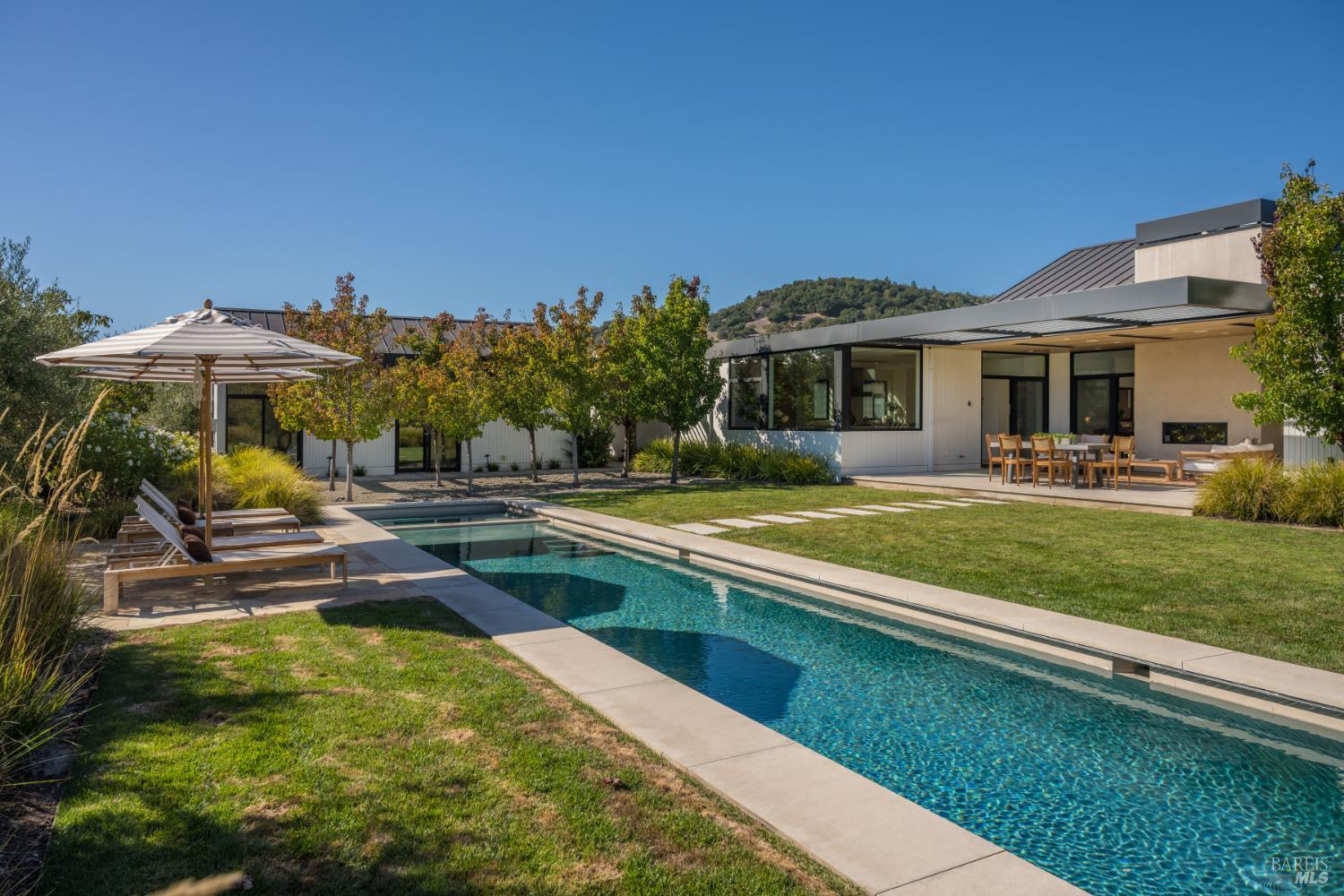 Modern Sonoma home beside a long swimming pool, with outdoor dining and wooded hills behind it.