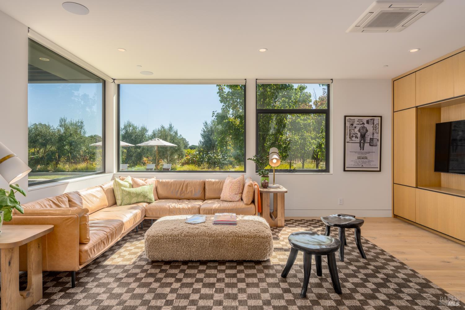 Living room with a tan leather sectional, expansive corner windows, and built-in wood media cabinetry.