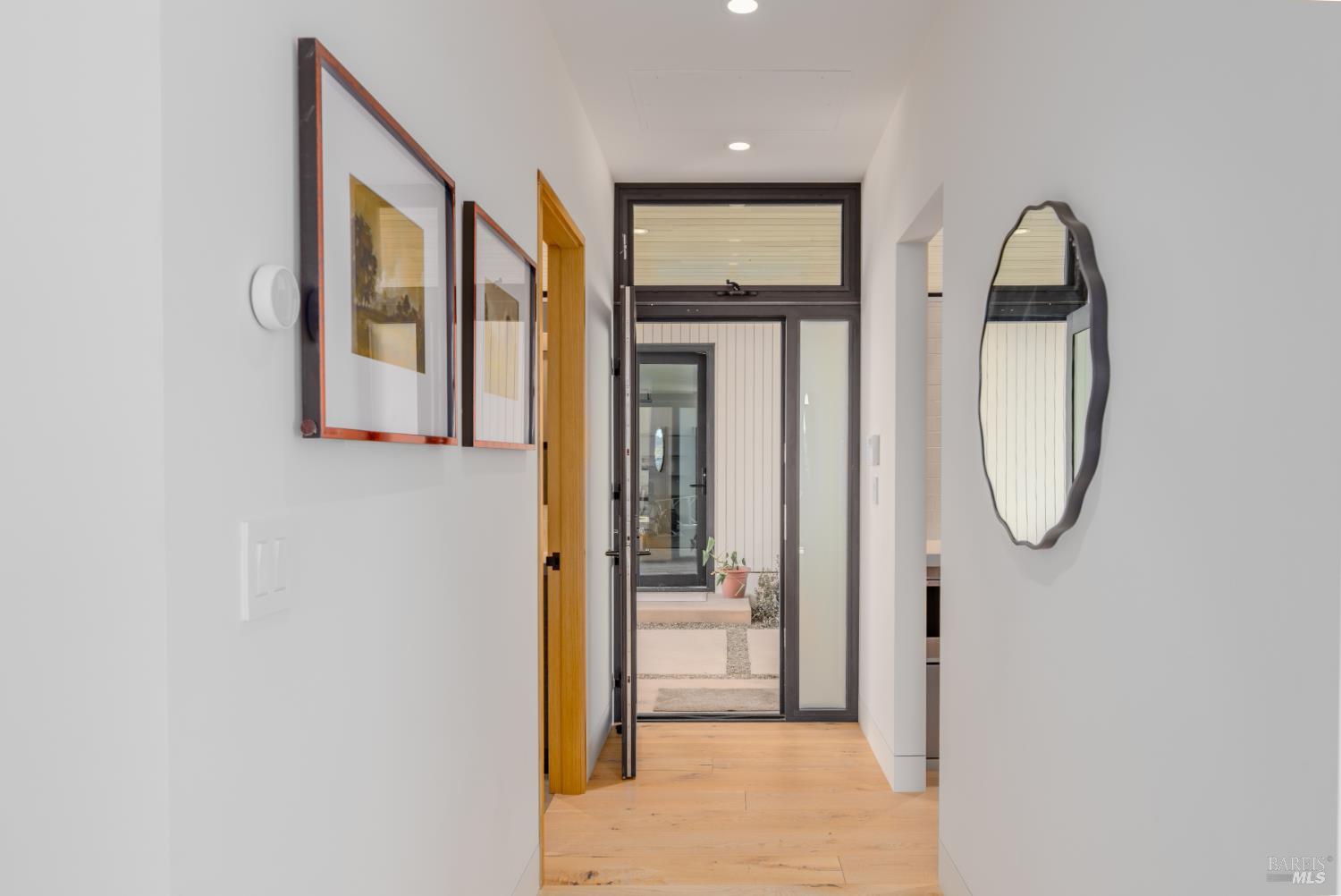 Modern entry hall with pale wood floors, framed artwork, and a dark-framed glass front door.