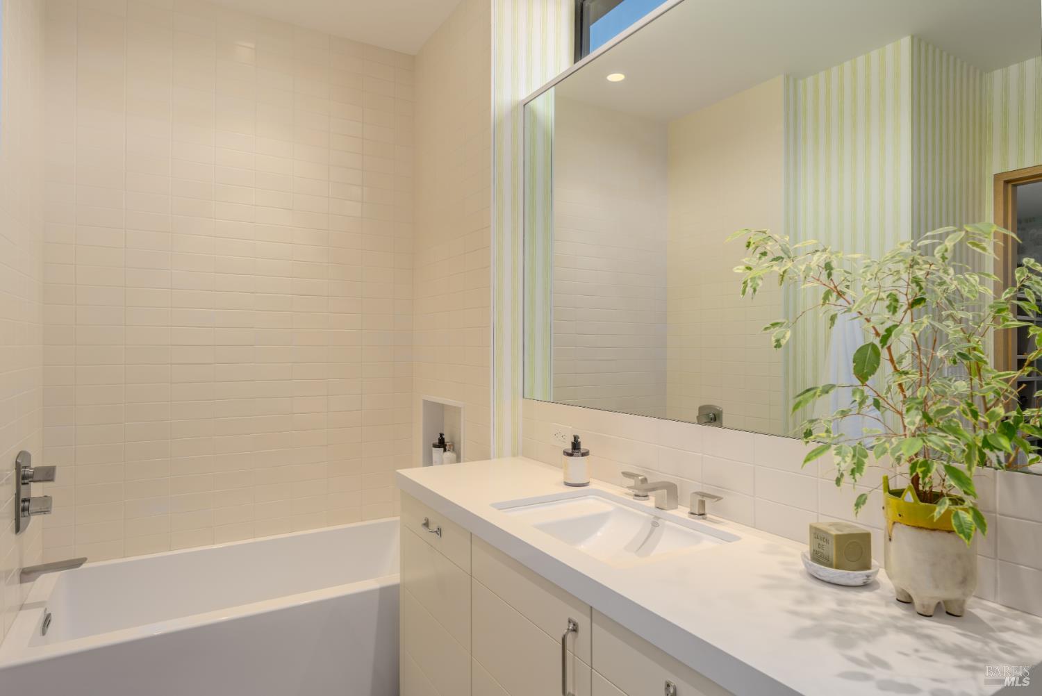 Bathroom with a white bathtub, double-sink vanity, large mirror, and potted plant.