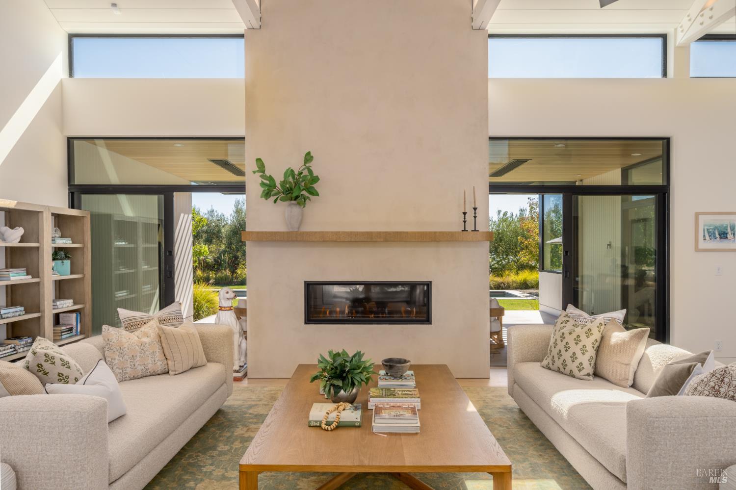 Living room with a tall central fireplace, cream sofas, and glass doors opening to a garden.