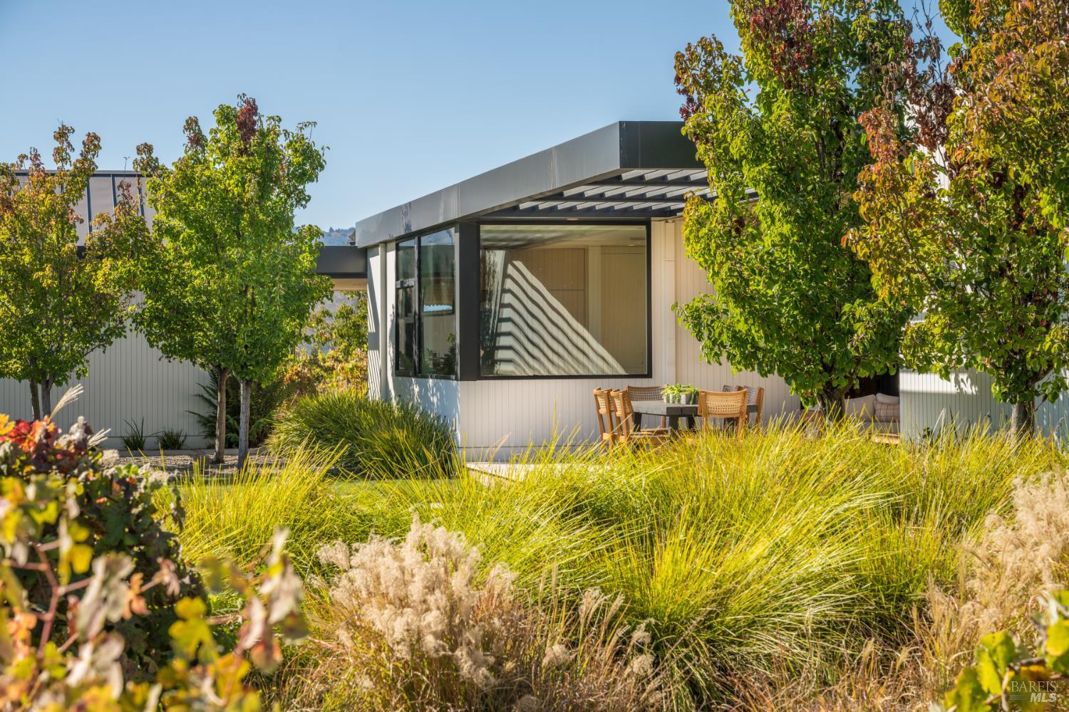 Modern home with a covered outdoor dining patio, large windows, and landscaped ornamental grasses.