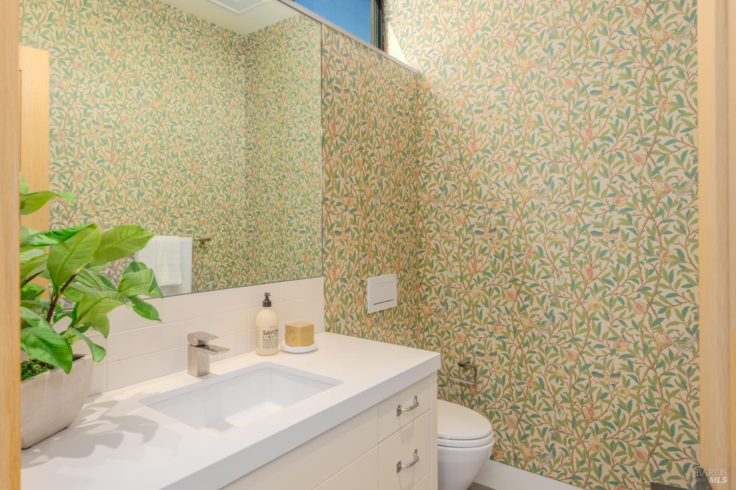 Bathroom with a white vanity, potted plant, and colorful floral wallpaper.