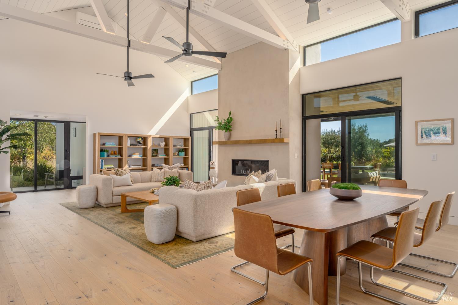 Open-plan living and dining room with vaulted beams, a fireplace, and large garden-facing glass doors.