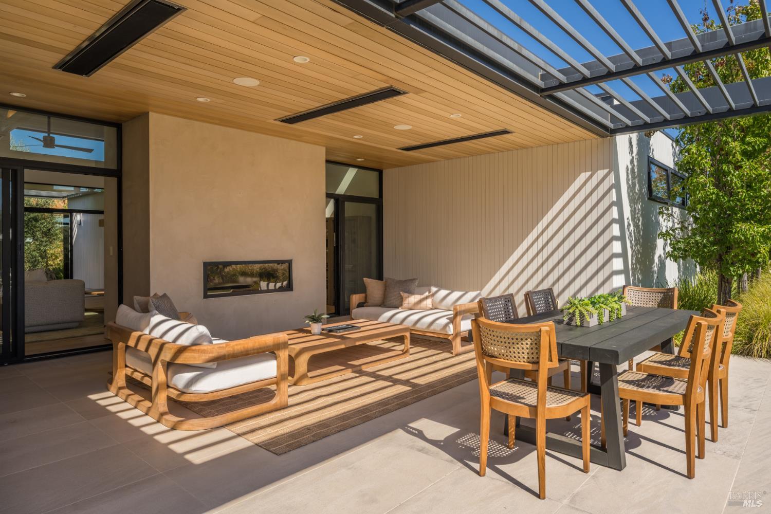 Covered patio with wood-framed lounge seating, dining table, linear fireplace, and open pergola.