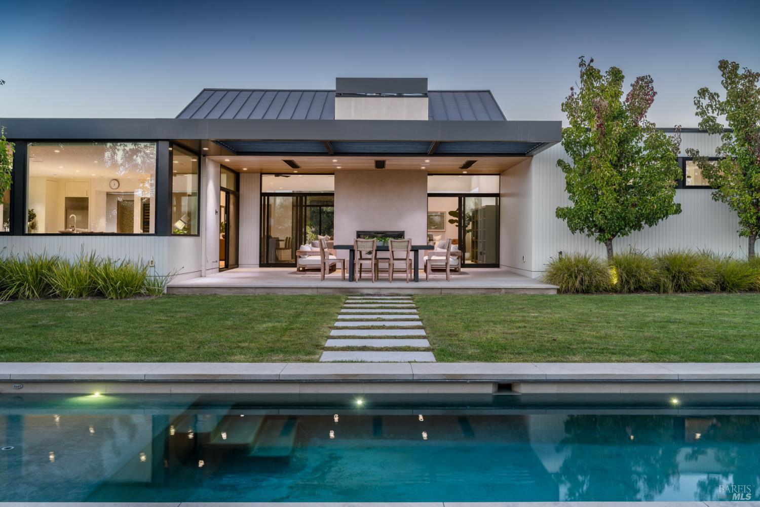Modern home with covered patio, lawn stepping-stone path, and swimming pool at dusk.