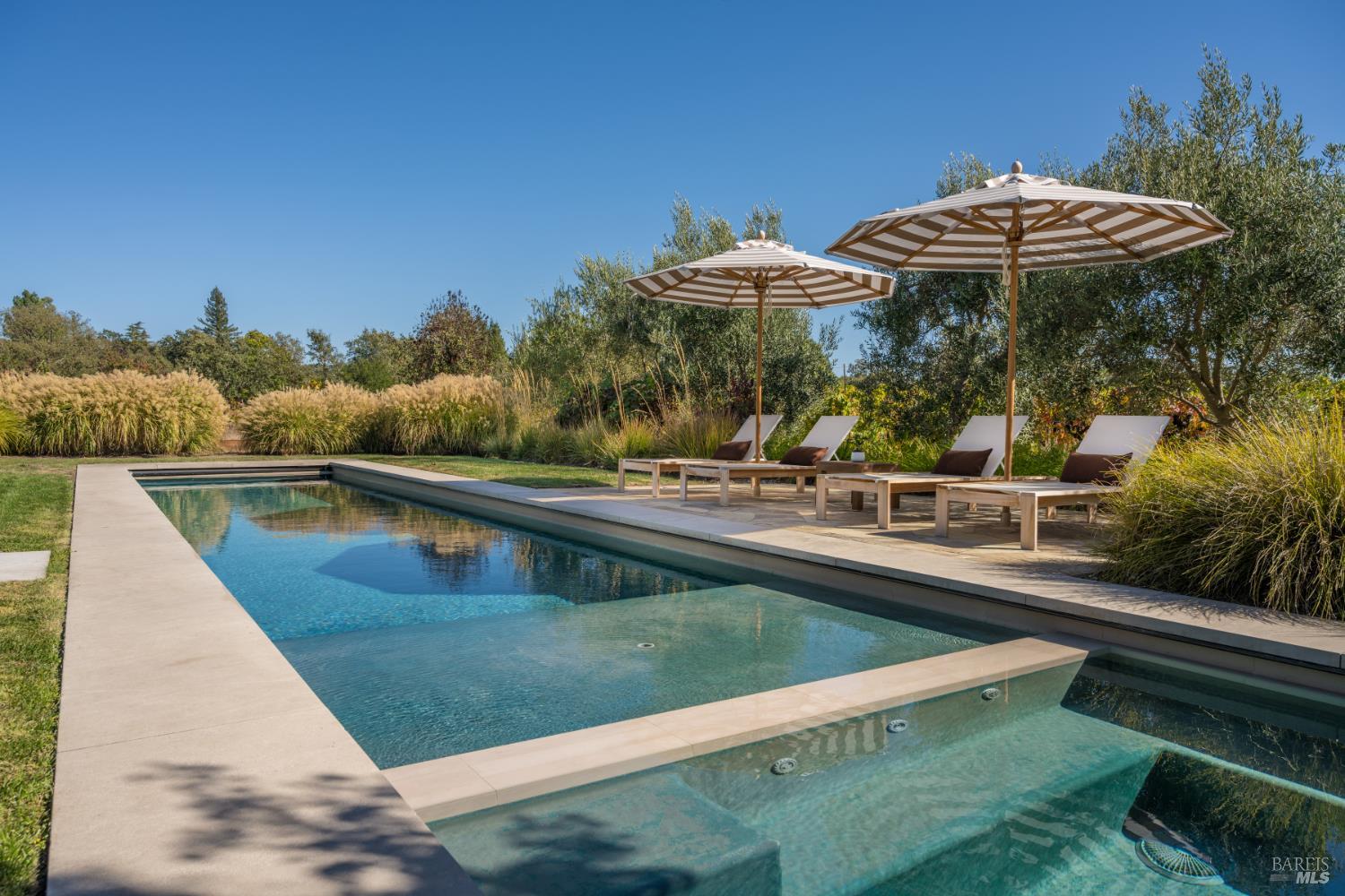 Outdoor pool with a shallow ledge, lounge chairs, and striped umbrellas