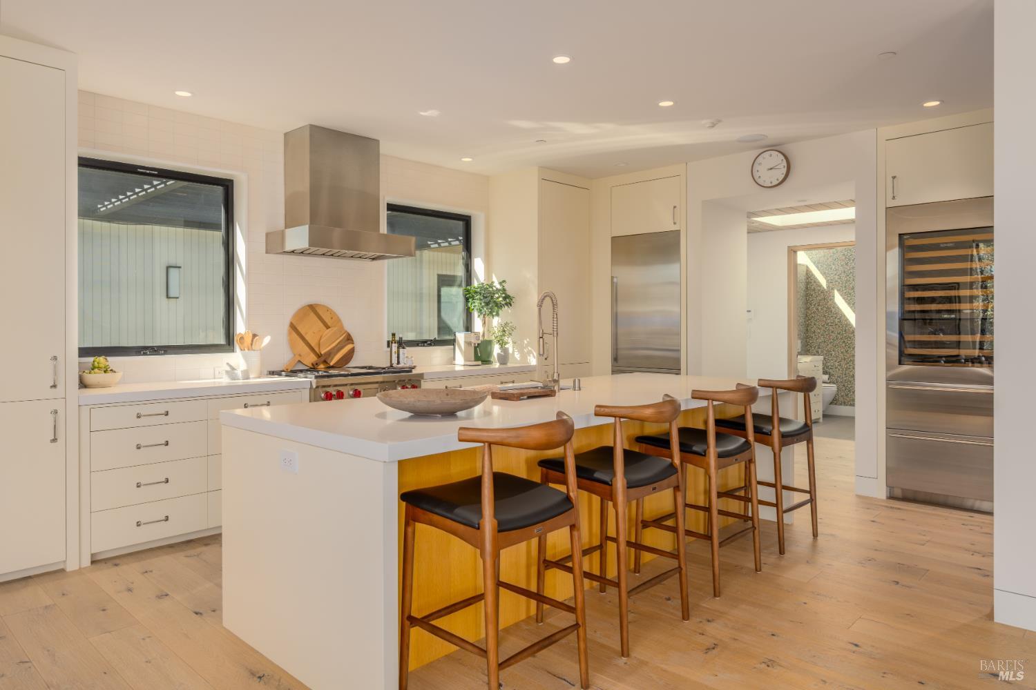 Modern kitchen with a large island, four bar stools, stainless steel appliances, and pale wood floors.