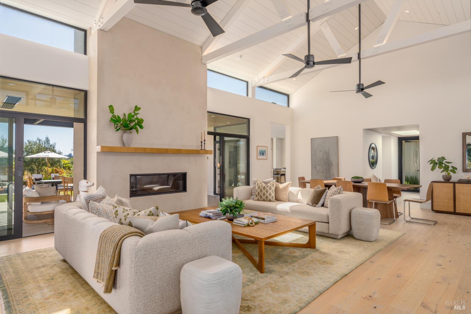 Open-plan living room with a linear fireplace, vaulted beamed ceiling, and sliding doors to a patio.