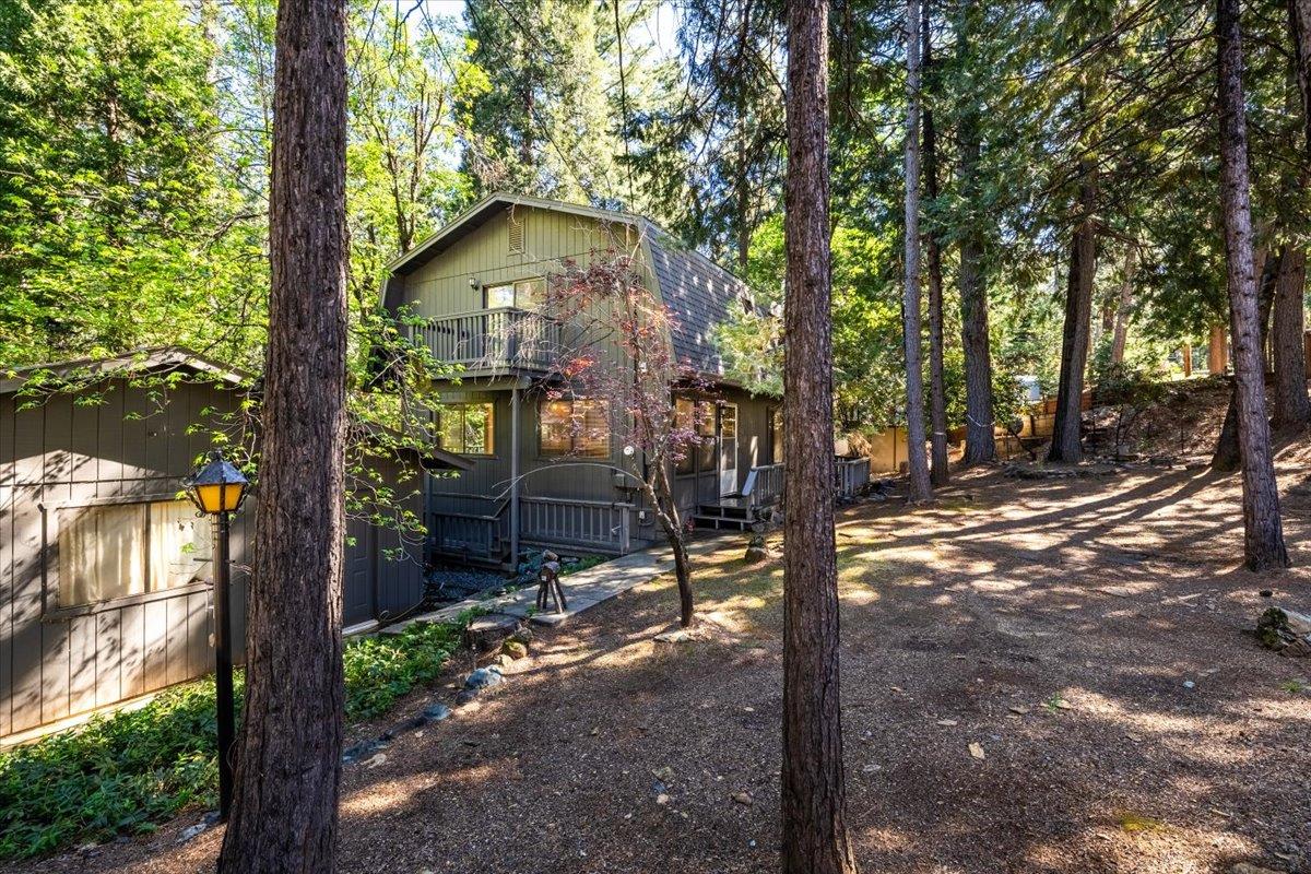 Dark gray two-story home with a balcony nestled among tall pine trees.
